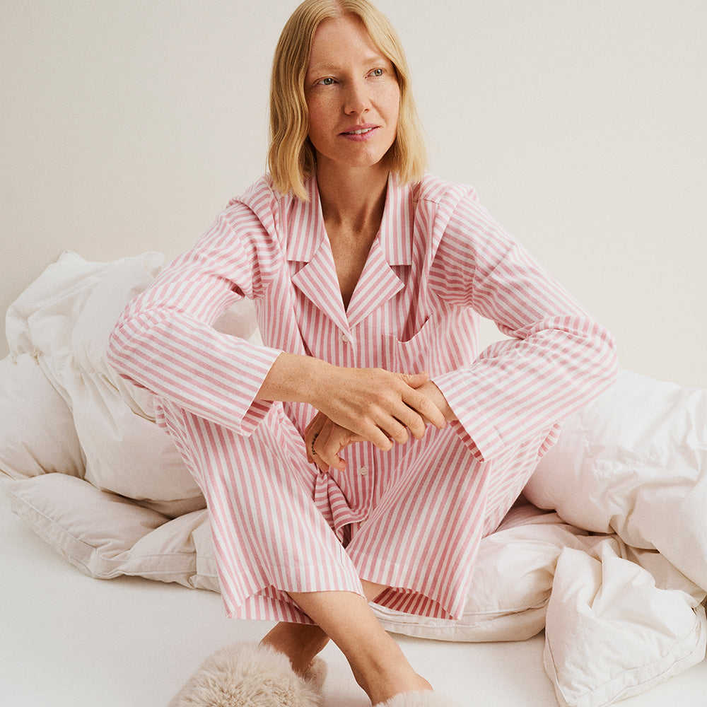 Woman wearing a Nanso pink and white striped Polka pyjama set sitting on a bed.