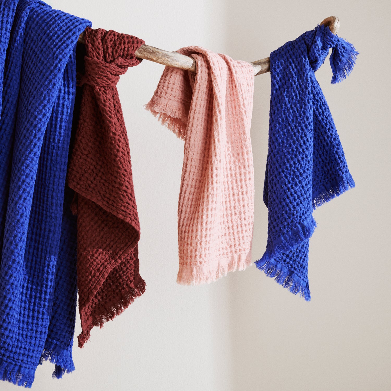 Four Vohveli towles in blue, red and pink hanging on a wooden rod against a light background.