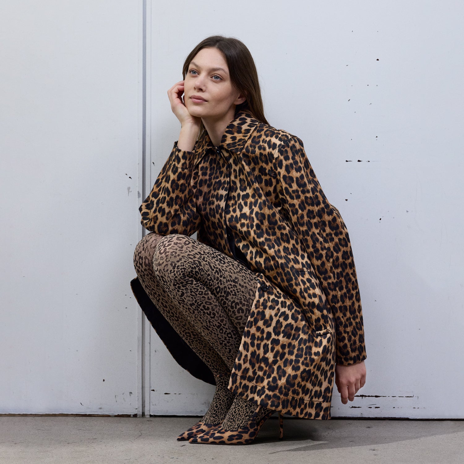 Woman wearing a leopard print outfit and matching Vogue tights sitting against a white wall.