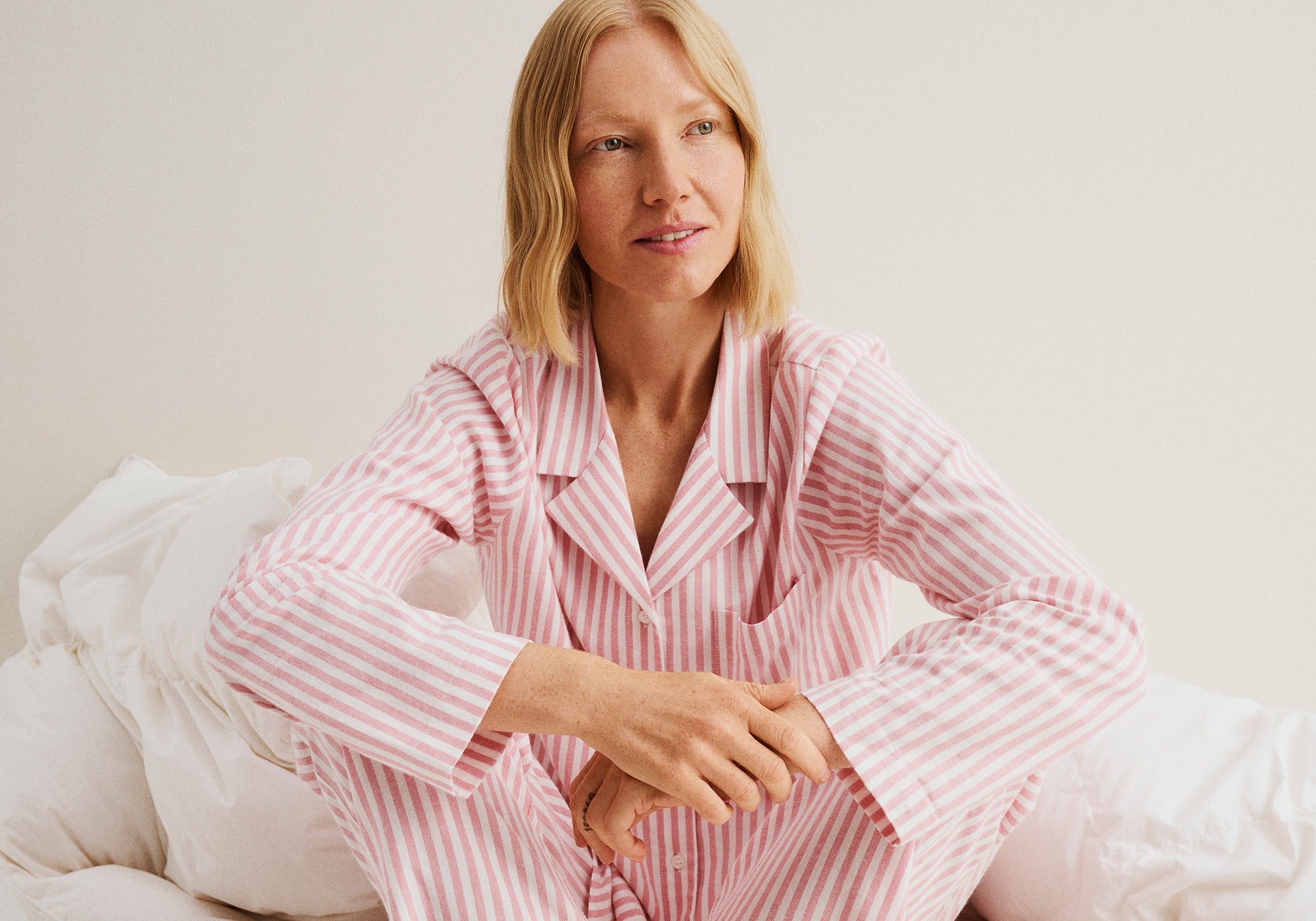 Woman wearing a Nanso pink and white striped Polka pyjama set sitting on a bed.