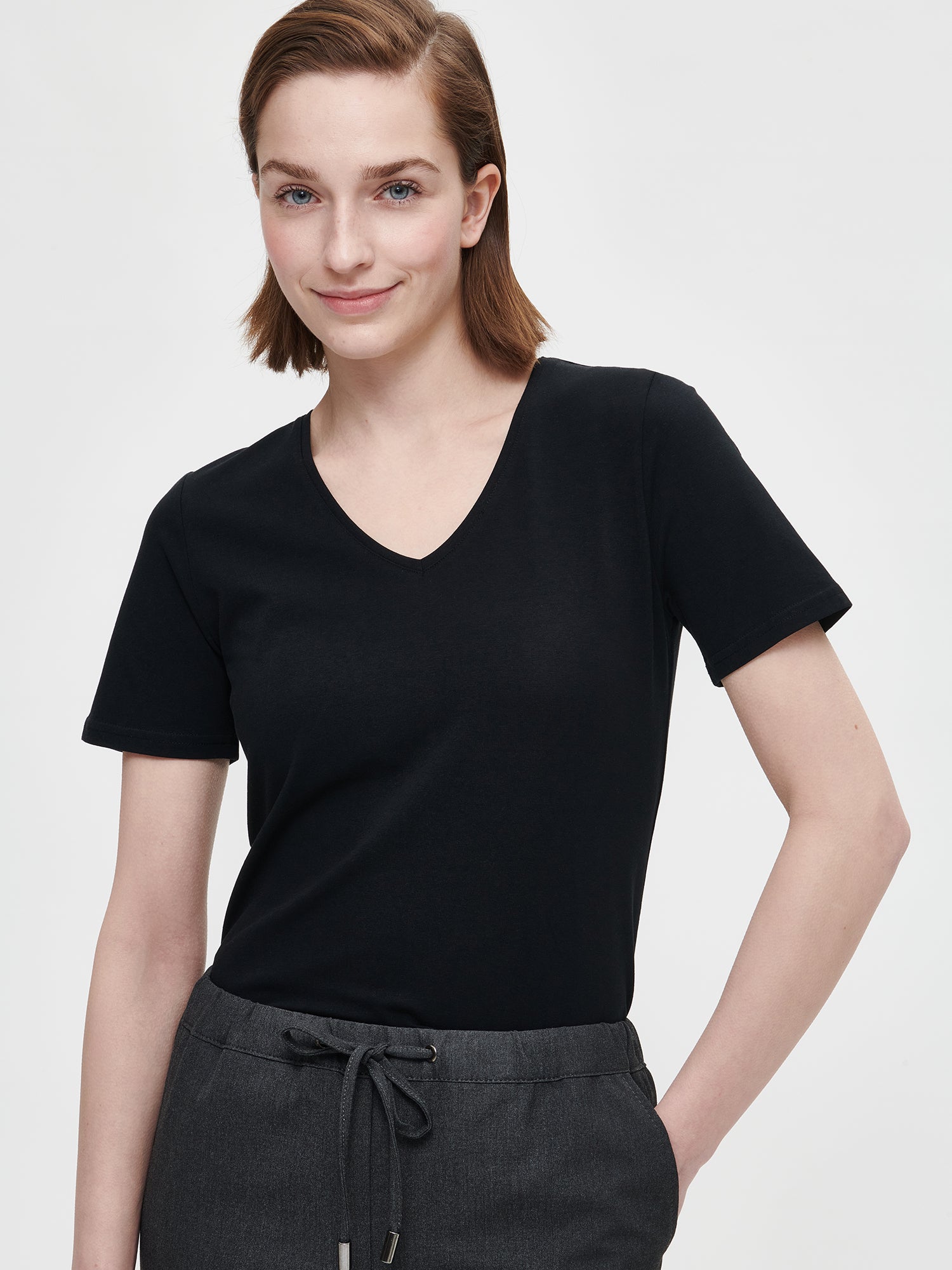 Women's Basic black T-shirt features a flattering V-neckline and comfortable short sleeves made from stretchy organic cotton-elastane blend, on a model pictured from the front.