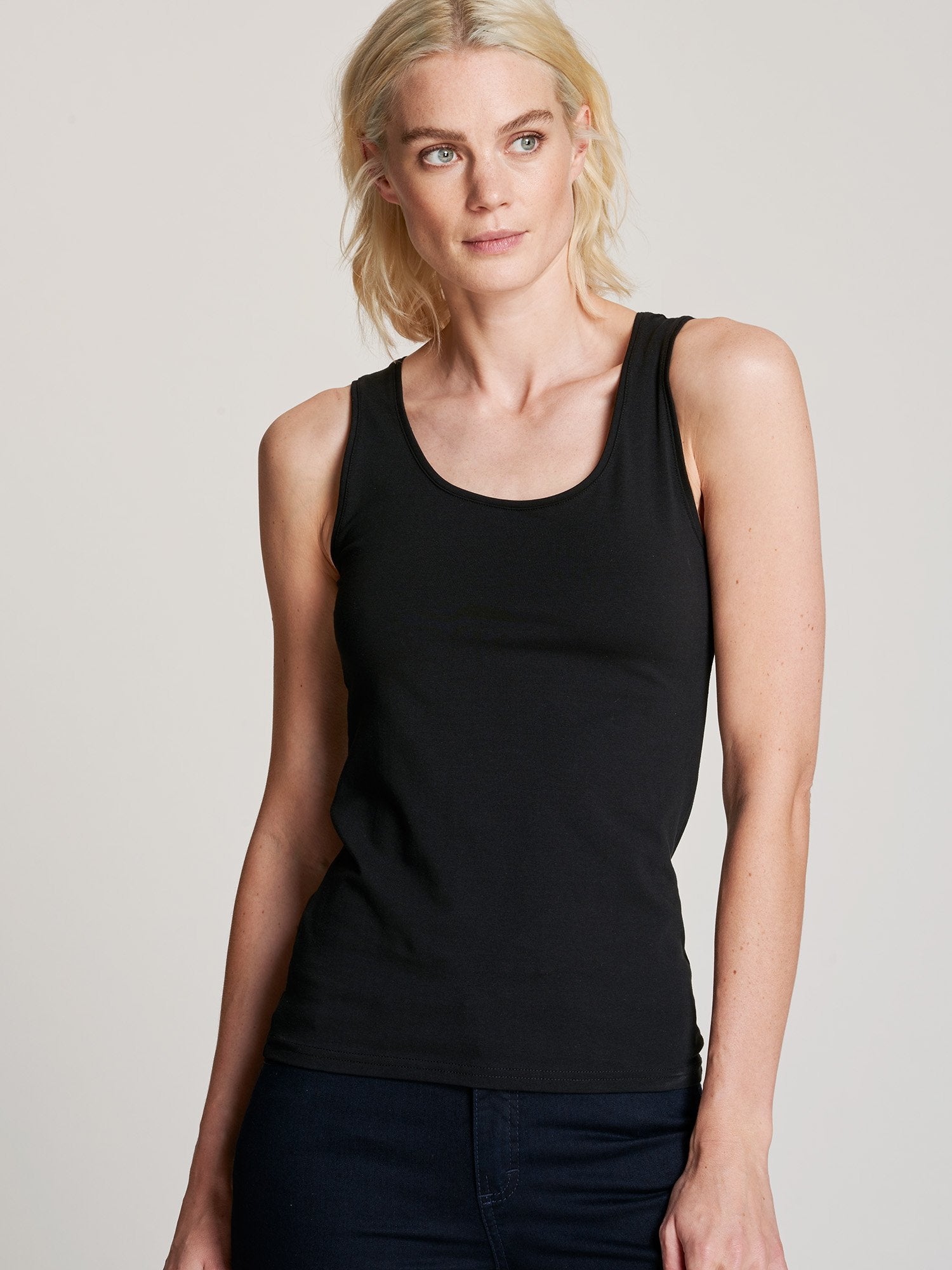 Nanso women's black Basic top with comfortable wide straps and a timeless silhouette. Crafted from soft, stretchy organic cotton-elastane knit. On a model with jeans, close up.