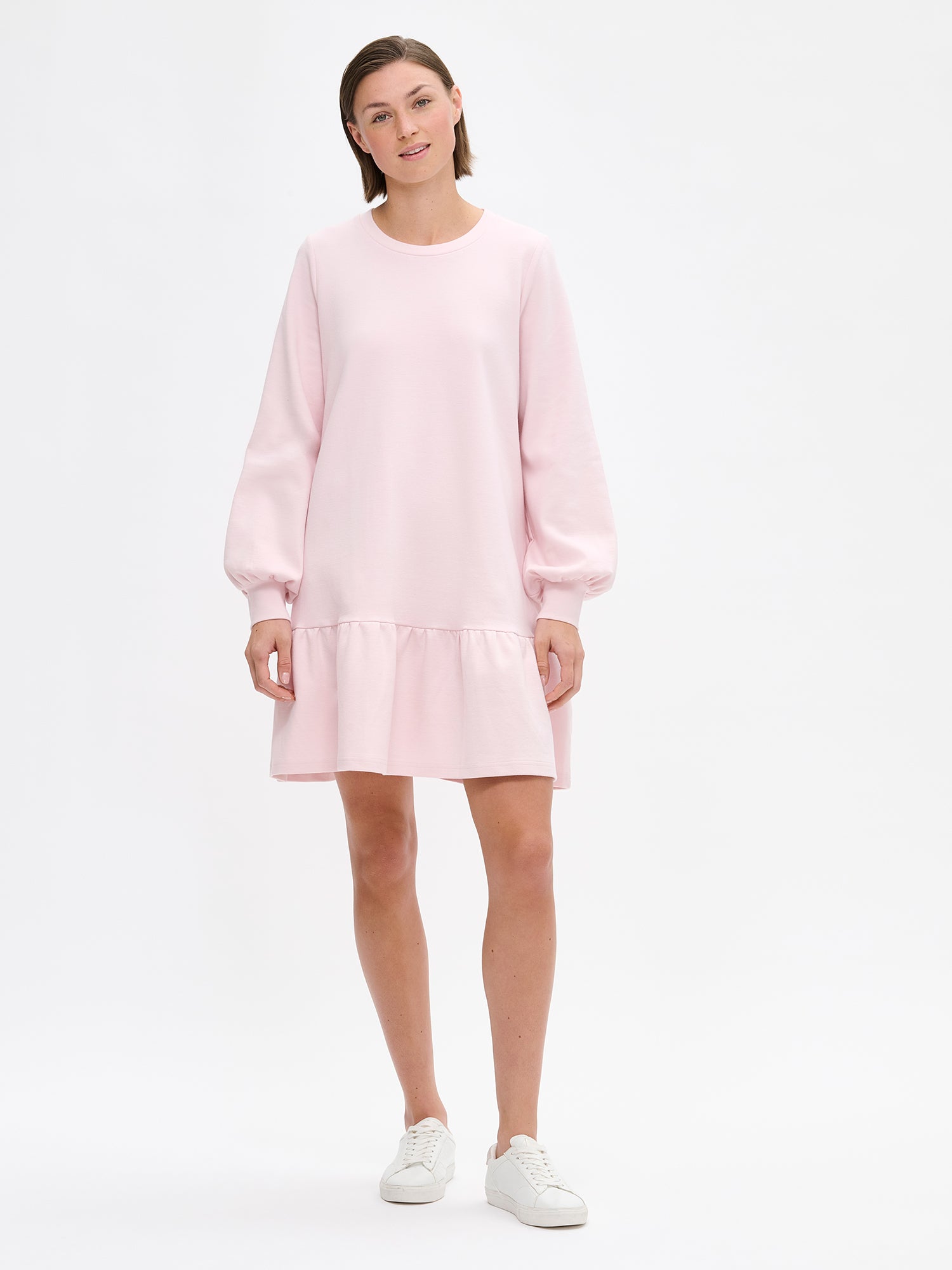 Nanso women's short casual Leija dress has a round neckline, pockets on the sides, a hem with pleats and full-length sleeves that gather beautifully at the cuffs. Pictured on a model with sneakers.
