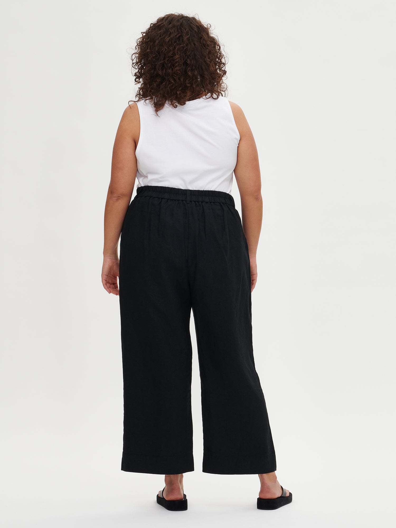 Saari linen culottes trousers in a lovely black shade for women with an elastic waistband and 7/8 length. These versatile pants are a staple for all seasons, perfect for both casual and formal occasions. Worn by a model in size 46 from the back.