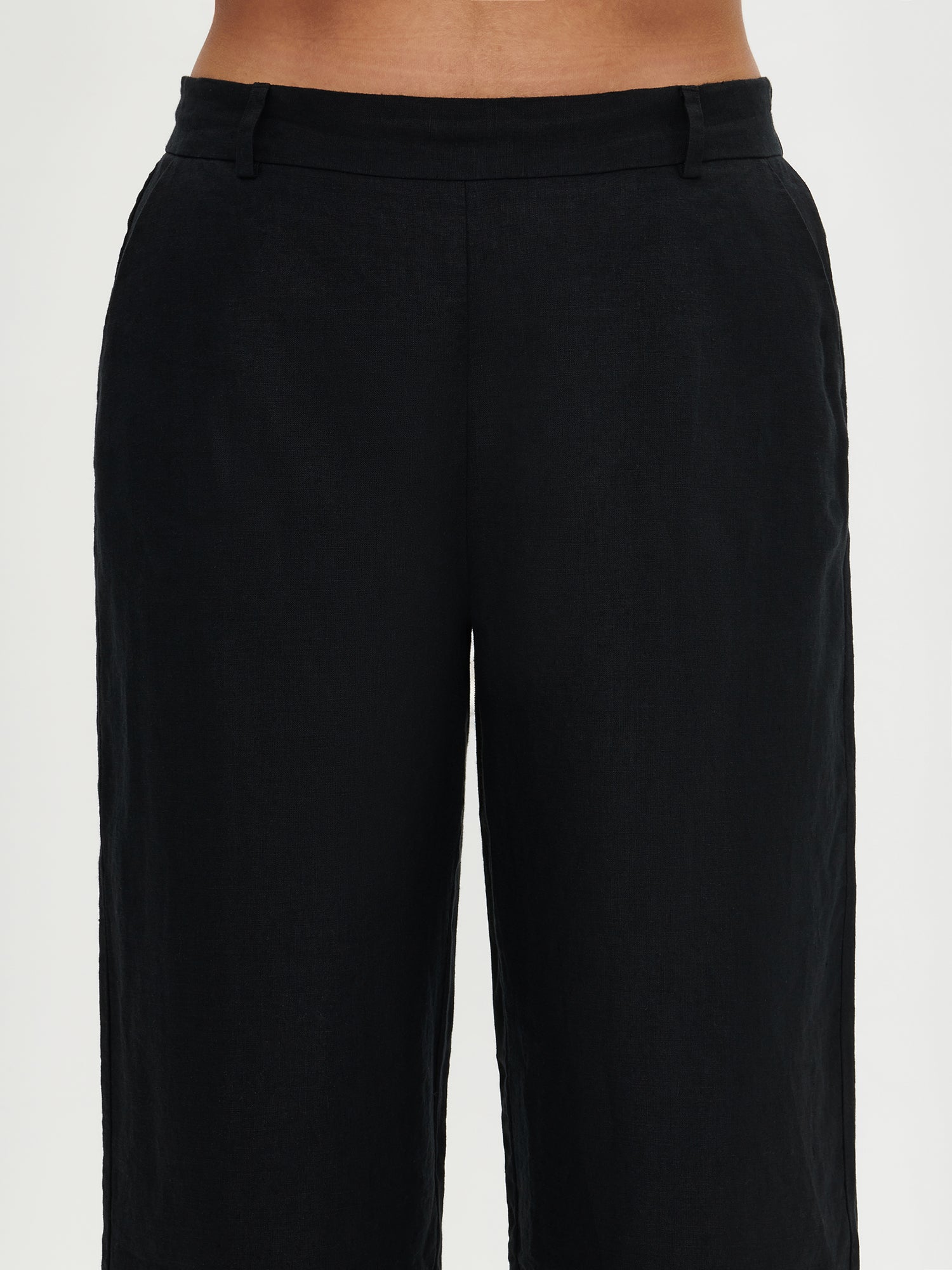 Saari linen culottes trousers in a lovely black shade for women with an elastic waistband and 7/8 length. These versatile pants are a staple for all seasons, perfect for both casual and formal occasions. Worn by a model from the front.
