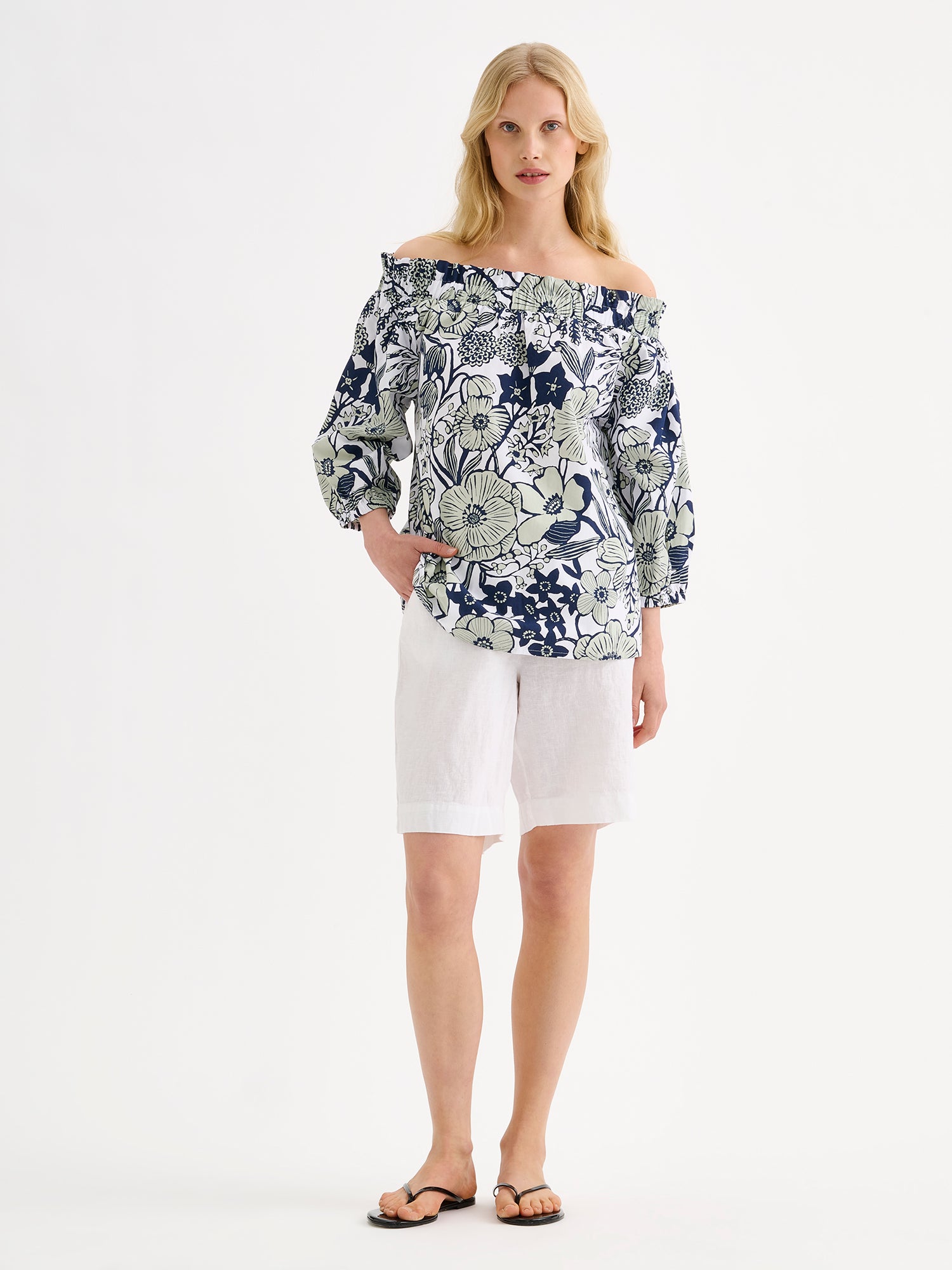 Nanso women's HUVILA Blouse with a charming floral print features a fresh, serene blue-green palette. pictured on a model with white shorts