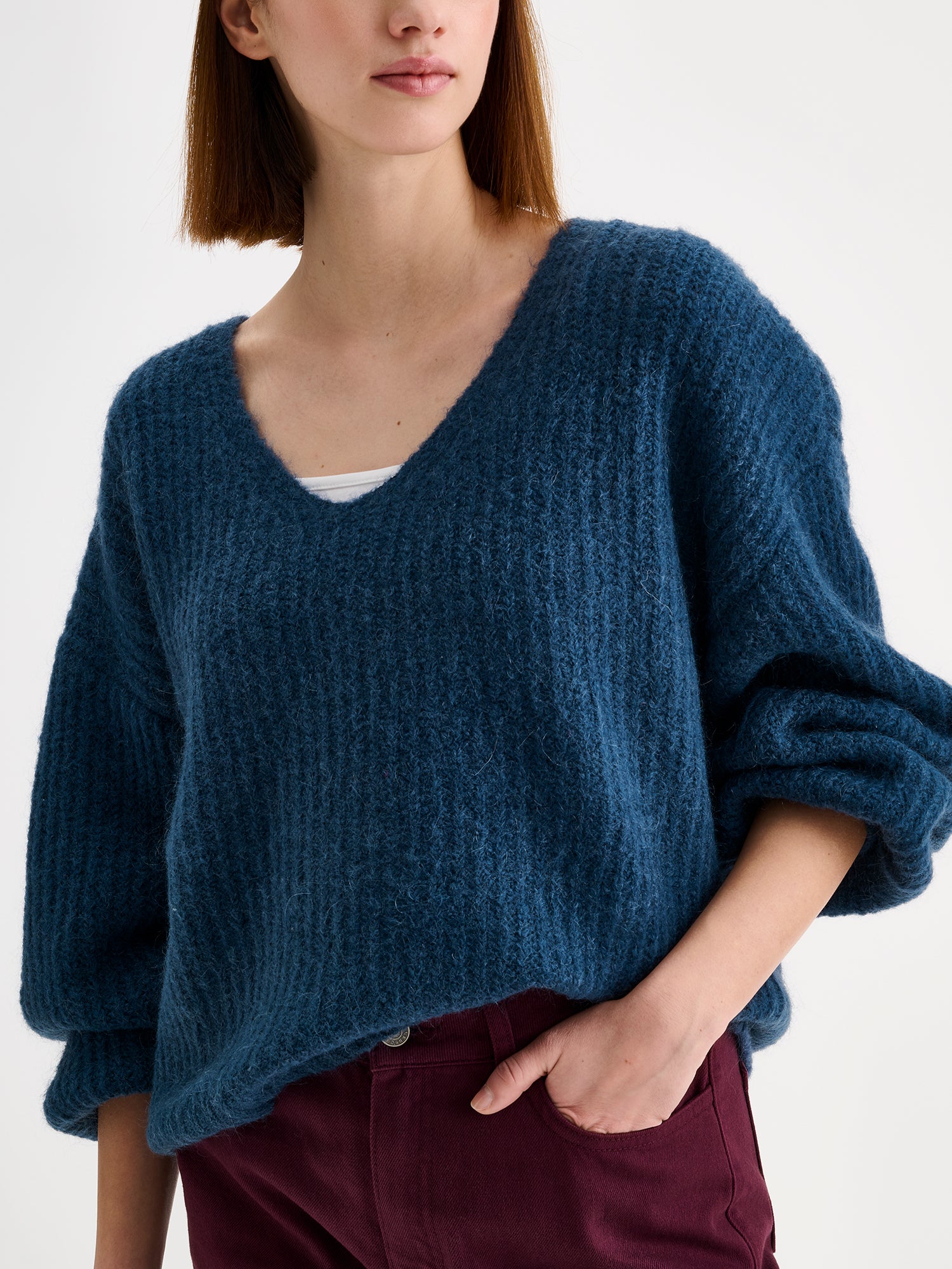 Nanso women's cozy blue Karamelli knit sweater with a V-neckline on a model with winered jeans, close-up.