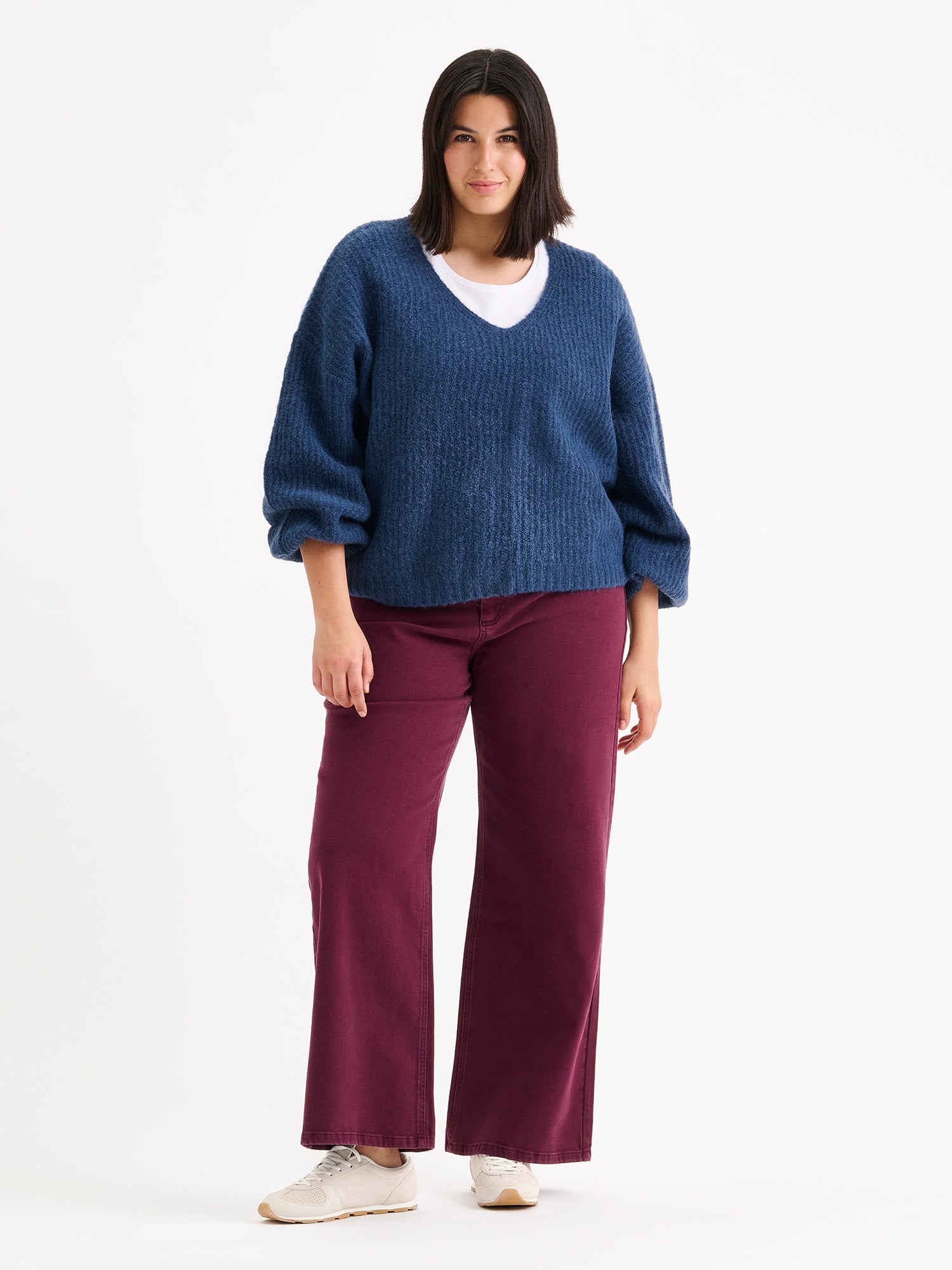 Nanso women's cozy blue Karamelli knit sweater with a V-neckline on a model with winered jeans.