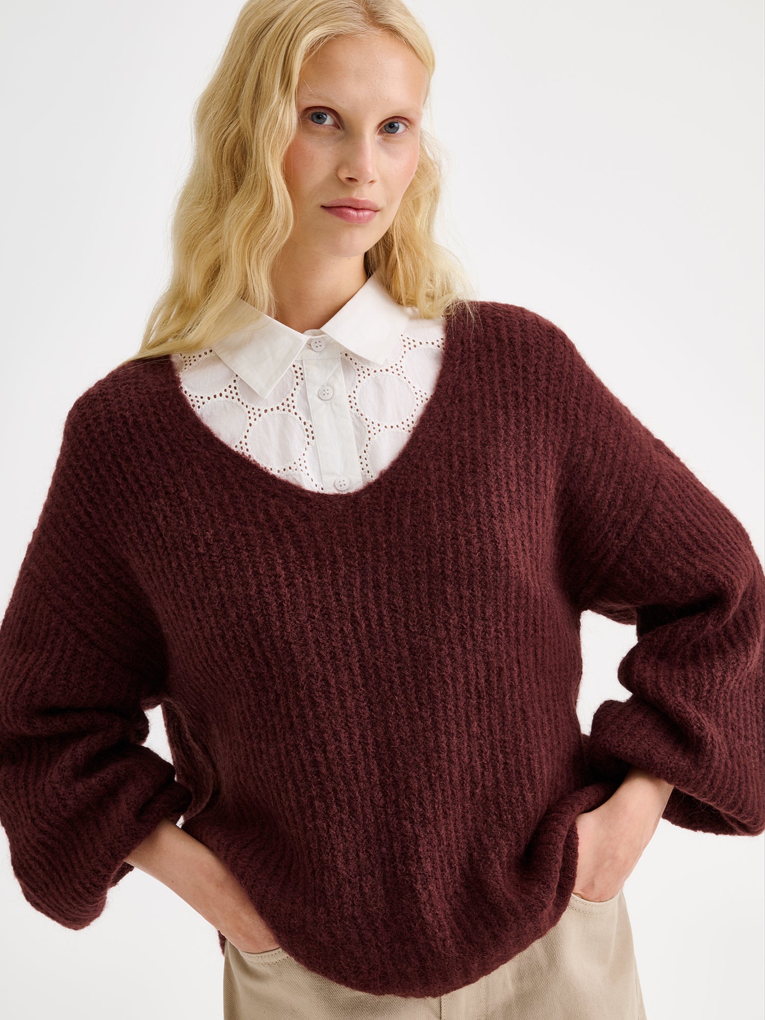 Nanso women's cozy dark brown Karamelli knit sweater with a V-neckline on a model with beige barrel jeans and a white shirt, close-up.