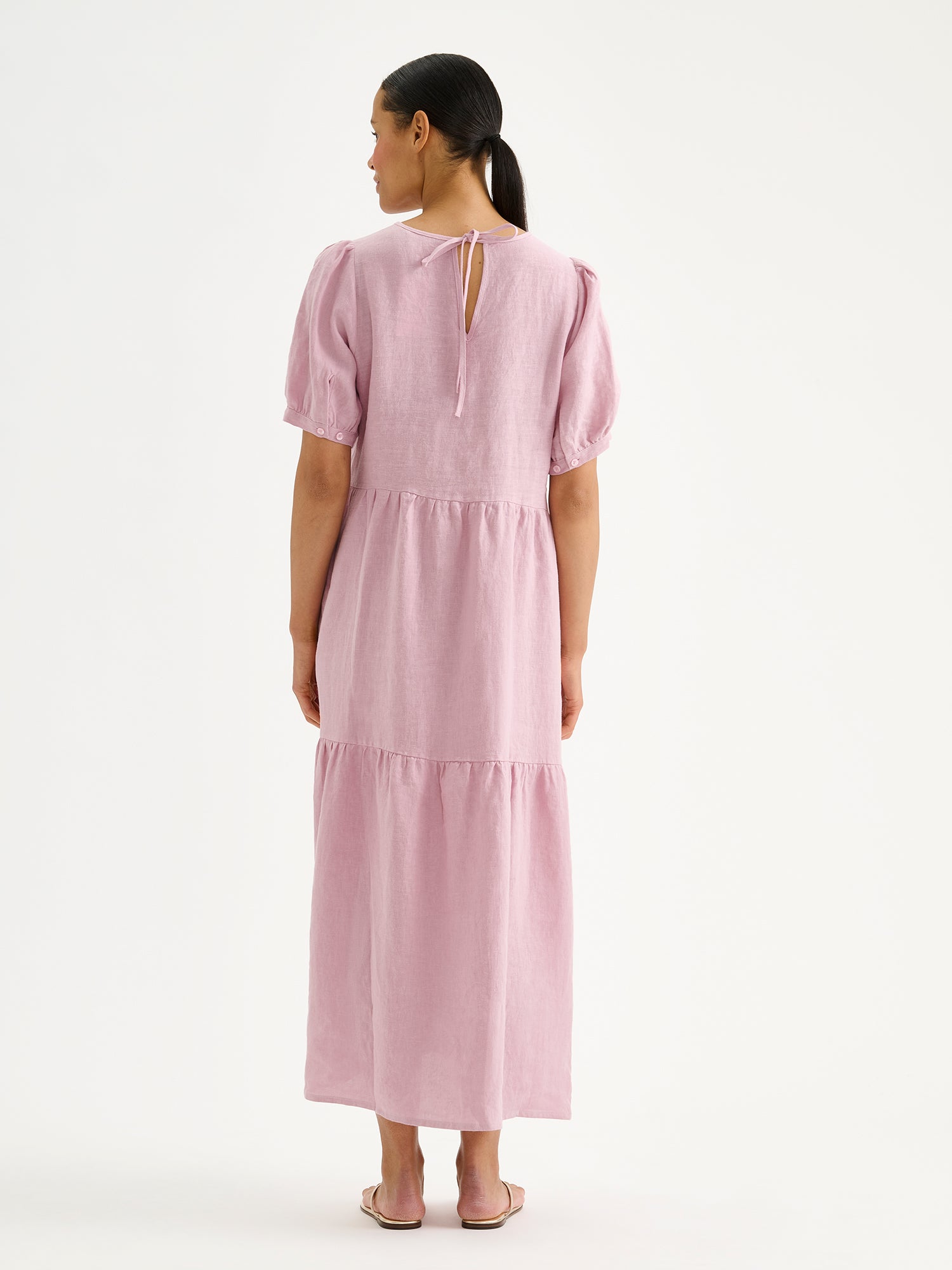 The Sarastus long lilac linen dress with voluminous frill layers and short puff sleeves on a model pictured from the backside.