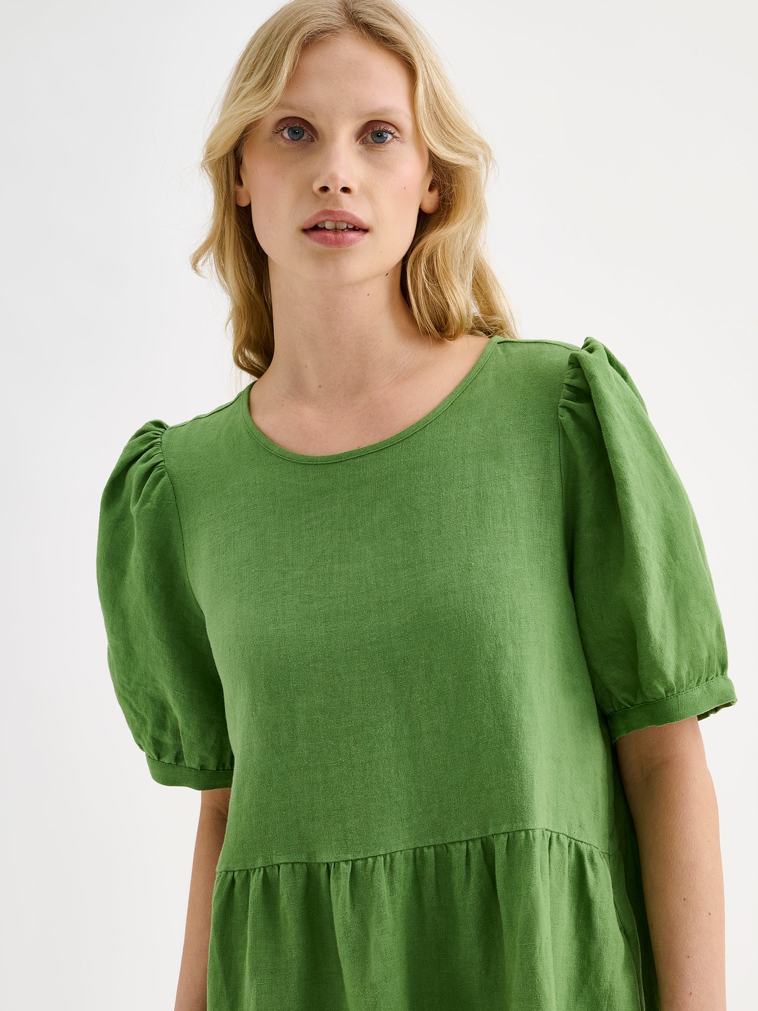 Nanso women's beautiful green Sarastus linen dress with voluminous frill layers and short puff sleeves on a model, close-up.