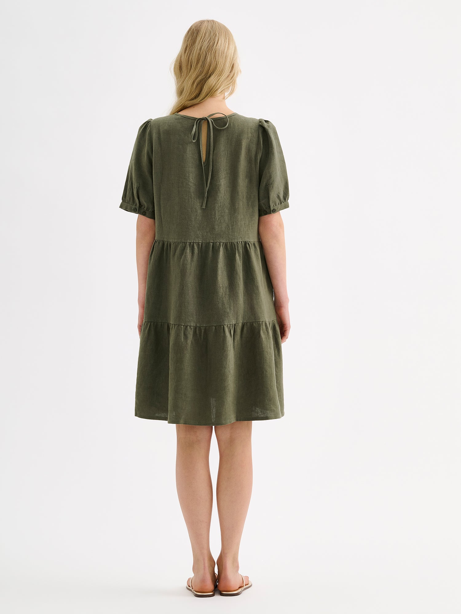 Nanso women's beautiful olive green Sarastus linen dress with voluminous frill layers and short puff sleeves on a blonde model, pictured from the backside