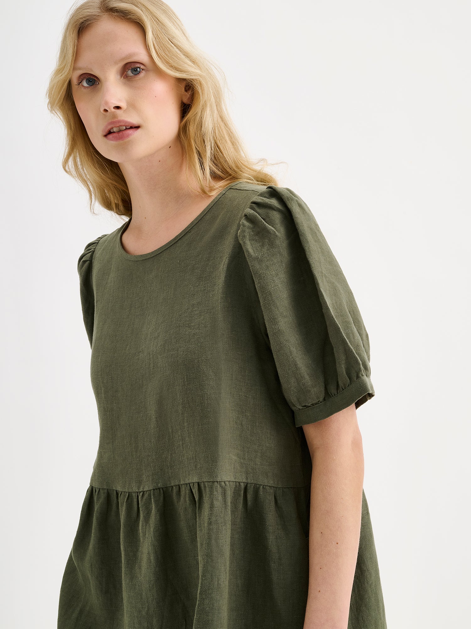 Nanso women's beautiful olive green Sarastus linen dress with voluminous frill layers and short puff sleeves on a blonde model, close-up.