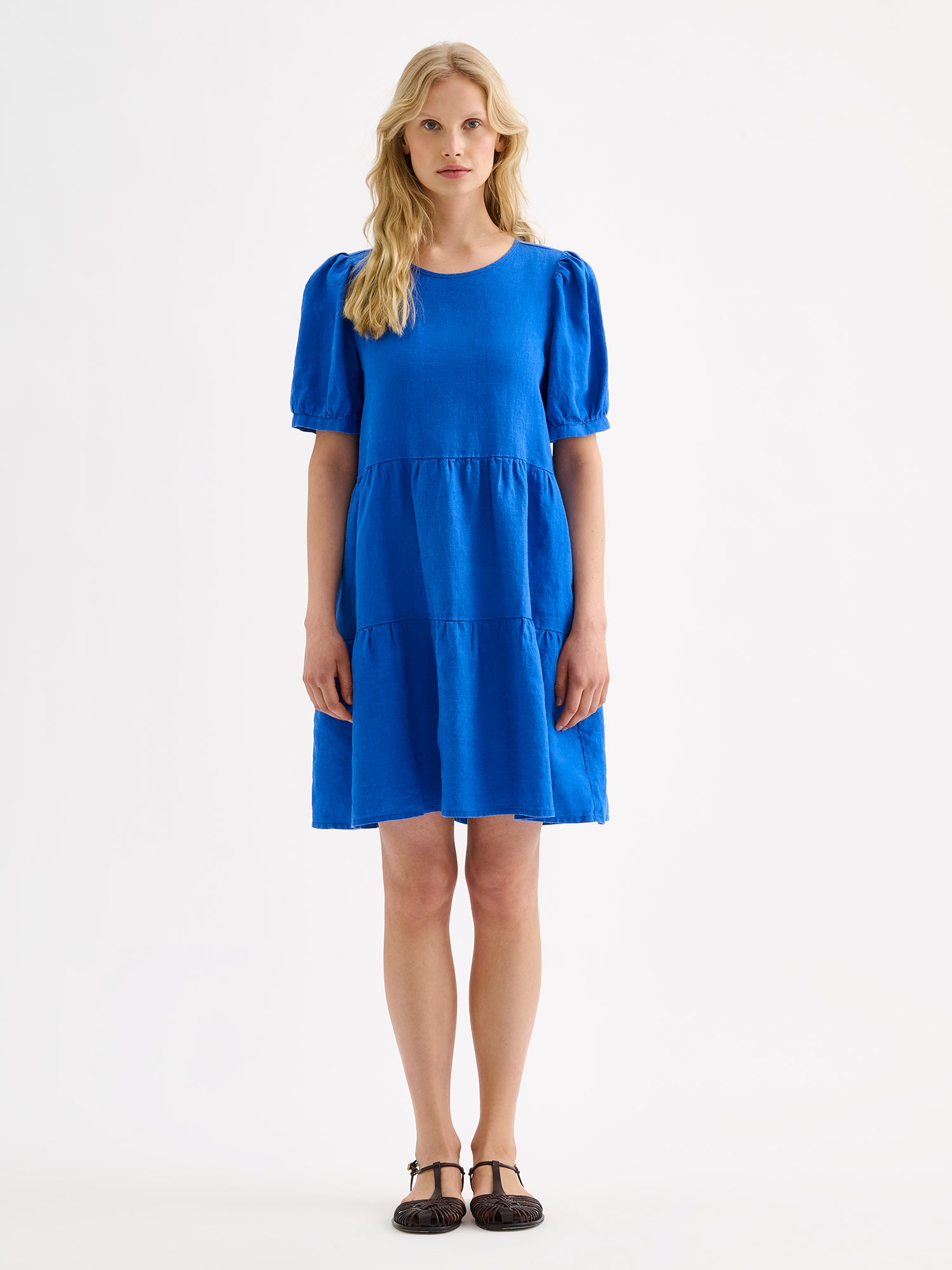 Nanso women's beautiful blue Sarastus linen dress with voluminous frill layers and short puff sleeves, on a model with sandals.