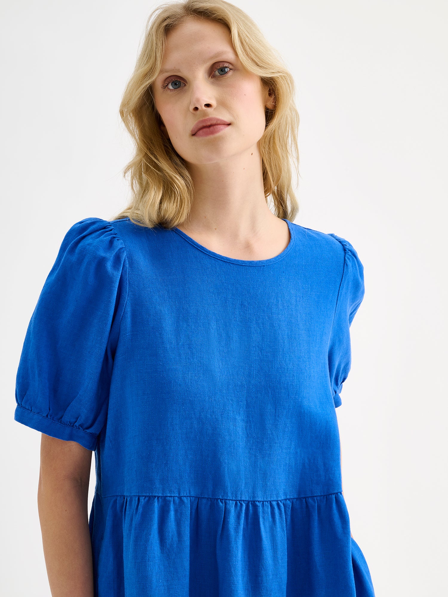 Nanso women's beautiful blue Sarastus midi linen dress features voluminous frill layers and short puff sleeves, on a model, close-up.
