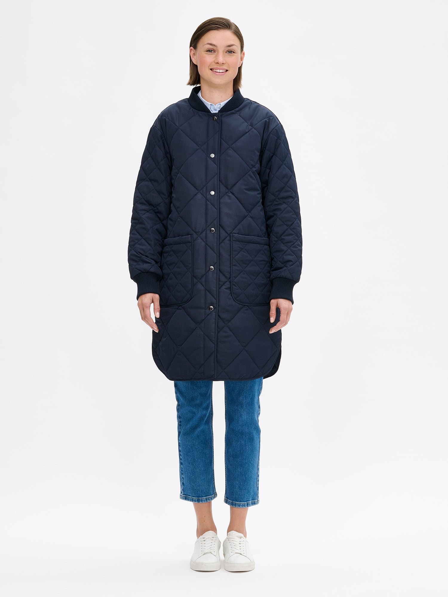 Nanso women's casual Midi quilted coat in dark blue features lightweight padding, ribbed knit detailing at the neckline and cuffs, snap closures and front pockets. Pictured on a model with jeans and sneakers.