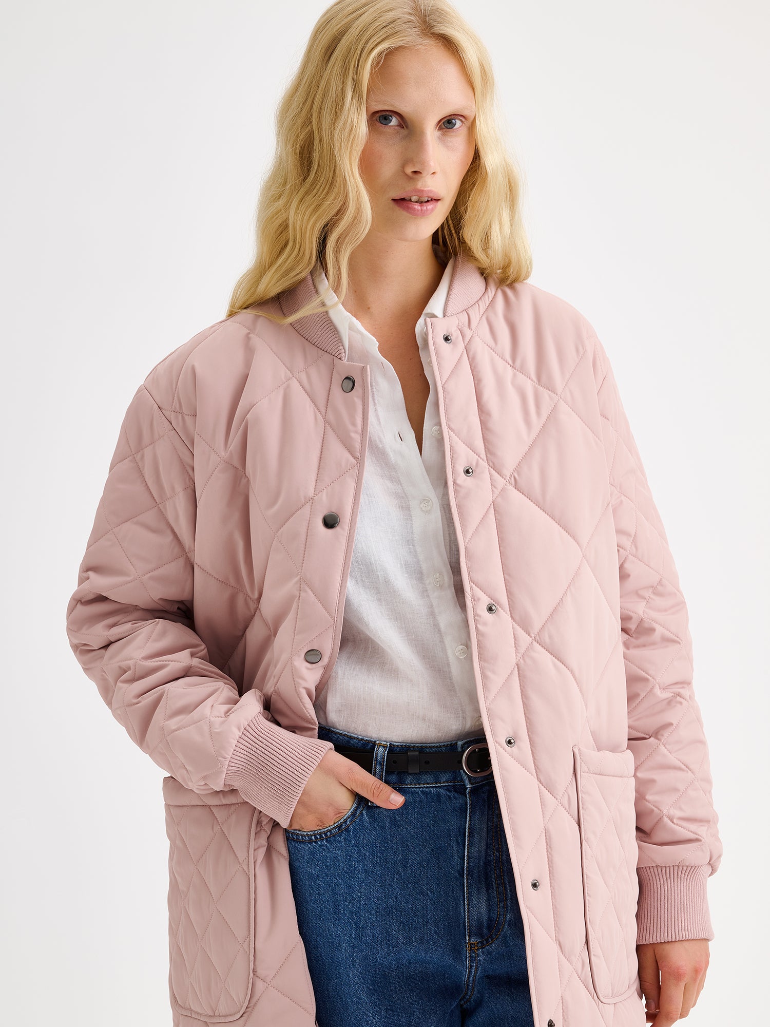 Nanso women's casual Midi quilted coat in dark blue features lightweight padding, ribbed knit detailing at the neckline and cuffs, snap closures and front pockets. Pictured on a model, coat opened, close-up.