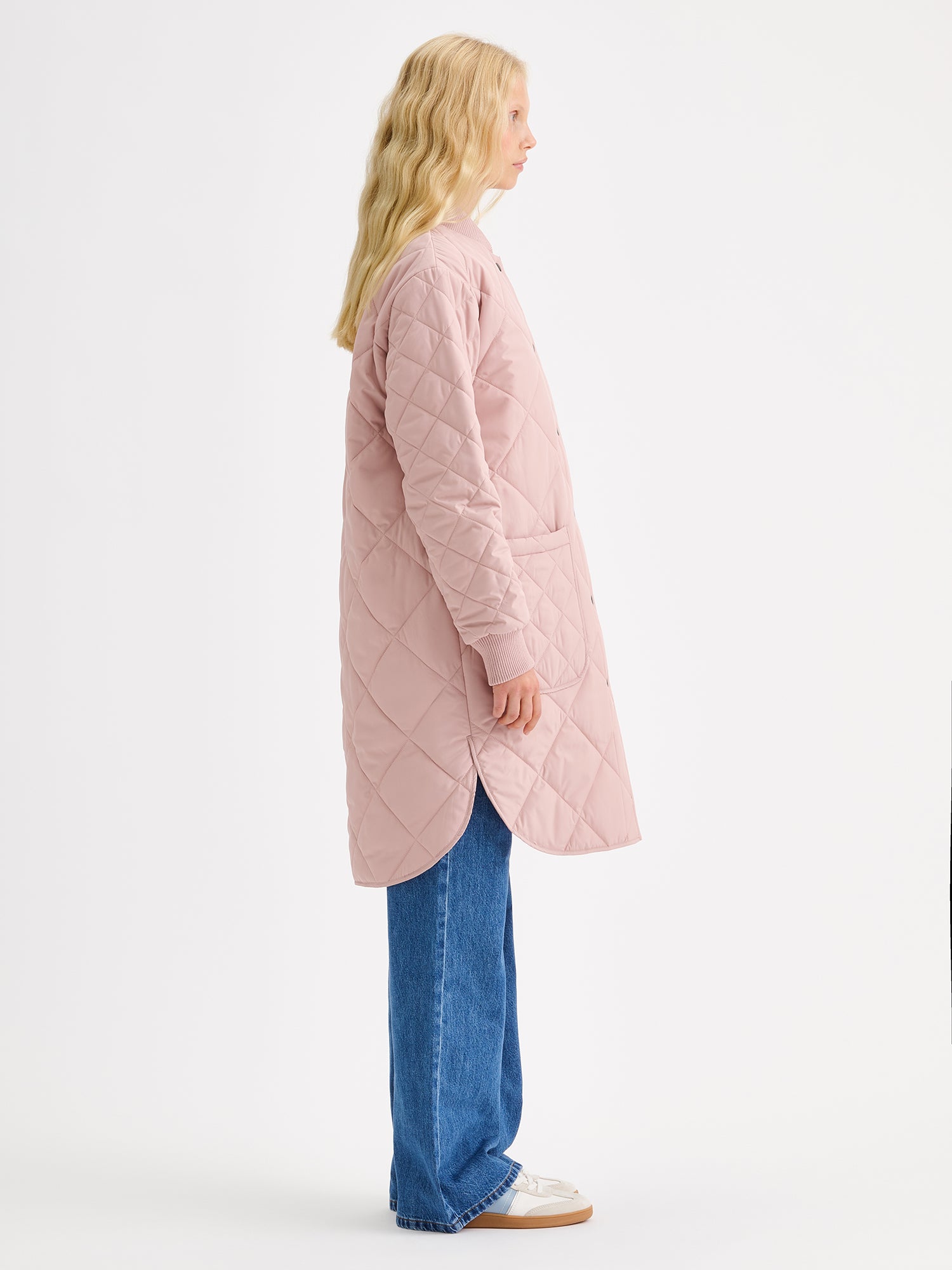 Nanso women's casual Midi quilted coat in dark blue features lightweight padding, ribbed knit detailing at the neckline and cuffs, snap closures and front pockets. Pictured on a model, from the side view.
