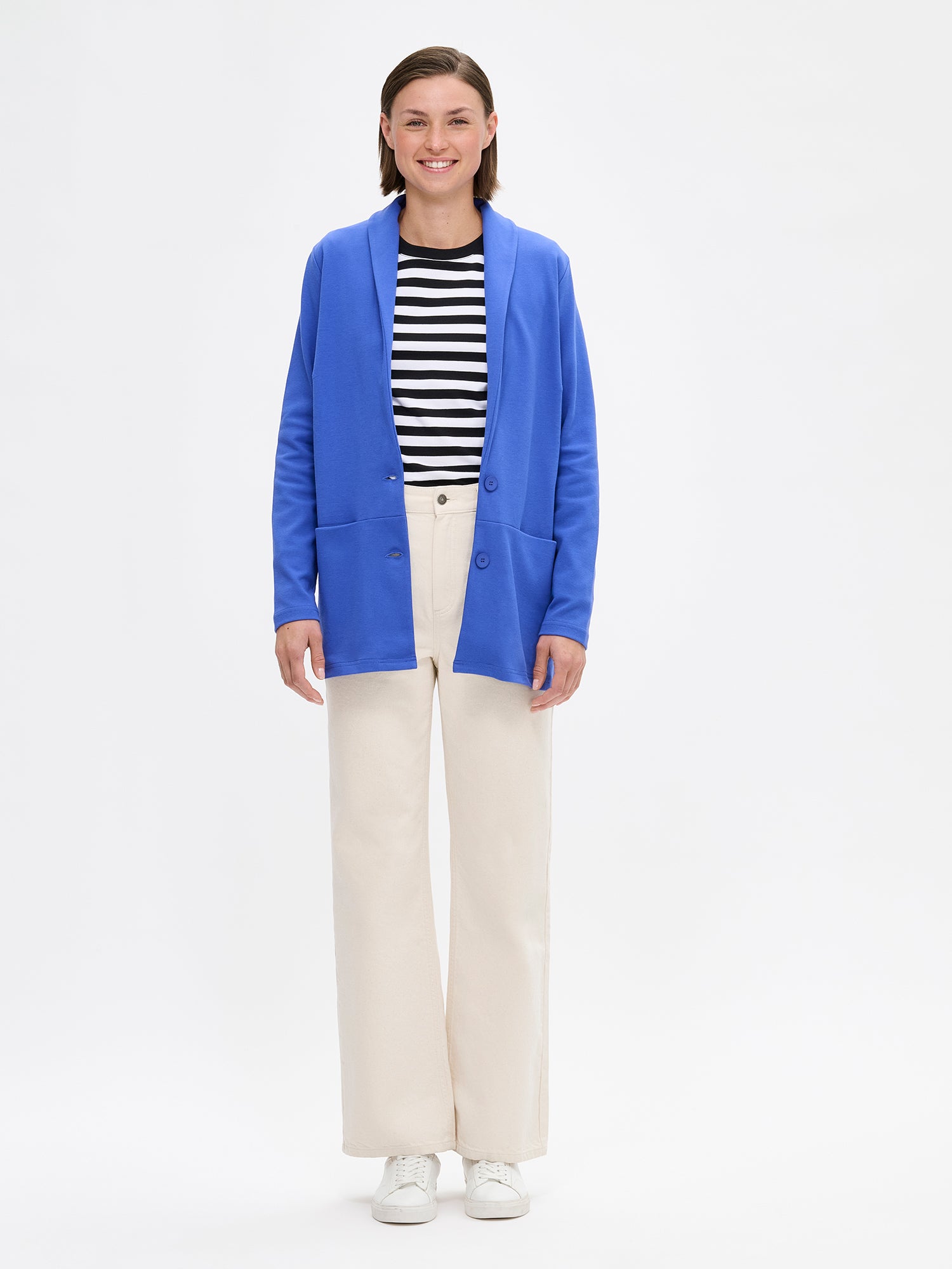 Nanso women's blue Leija jacket features a collar, front button closure, and bust darts. Sleeves are full-length. The front horizontal seam has embedded pockets. Pictured on a model with jeans and sneakers.