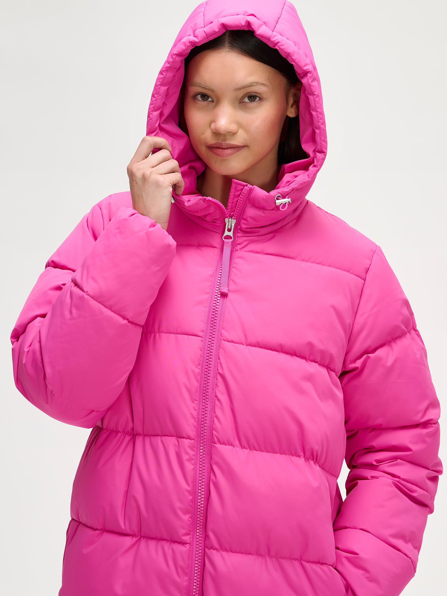 Nanso women´s Lumi Long Pink Puffer Coat in pink offers cozy warmth with its lightweight, puffy insulation. Worn by a model and the hood on.