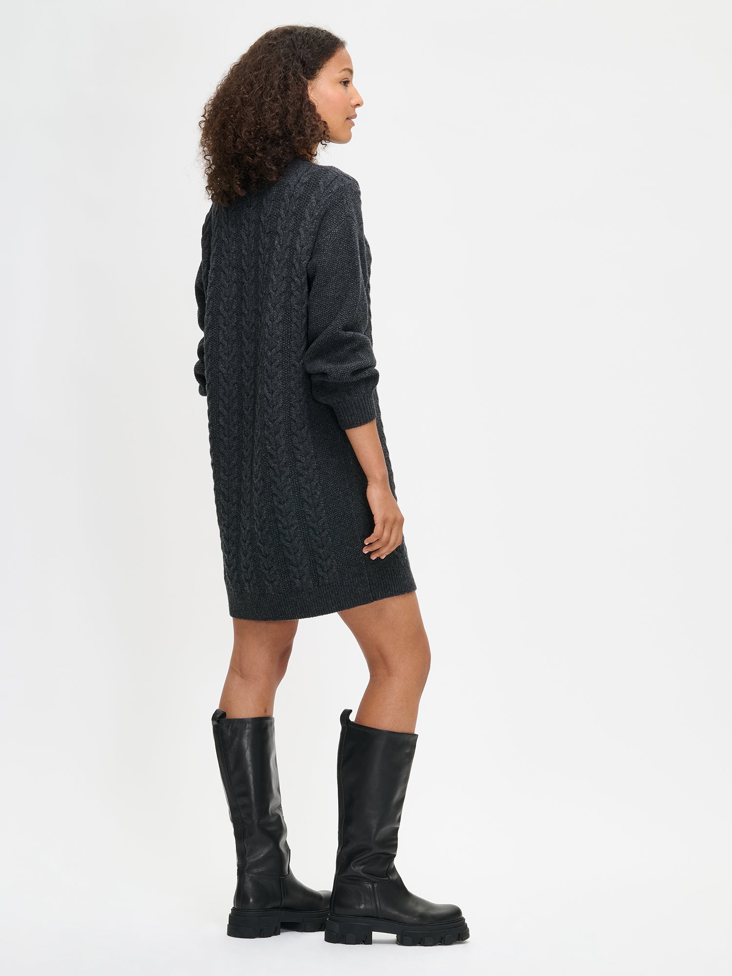 Woman wearing a dark gray cable knit dress with black knee-high boots on a white background