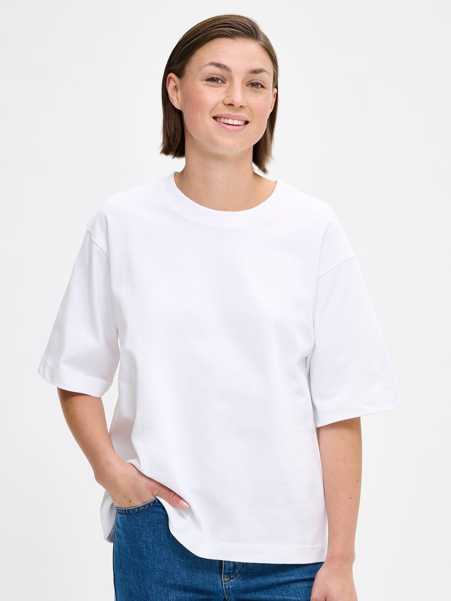 Nanso women's solid white Forma T-shirt. This boxy, loose-fitting T-shirt features a round ribbed neckline and loose 2/4-length sleeves. On a model with jeans, close-up.