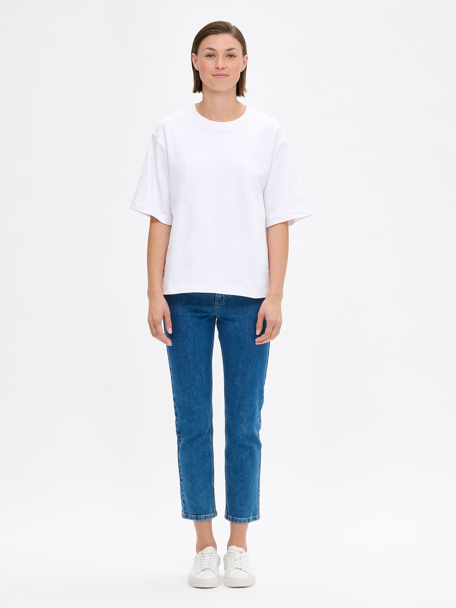 Nanso women's solid white Forma T-shirt. This boxy, loose-fitting T-shirt features a round ribbed neckline and loose 2/4-length sleeves. On a model with jeans.