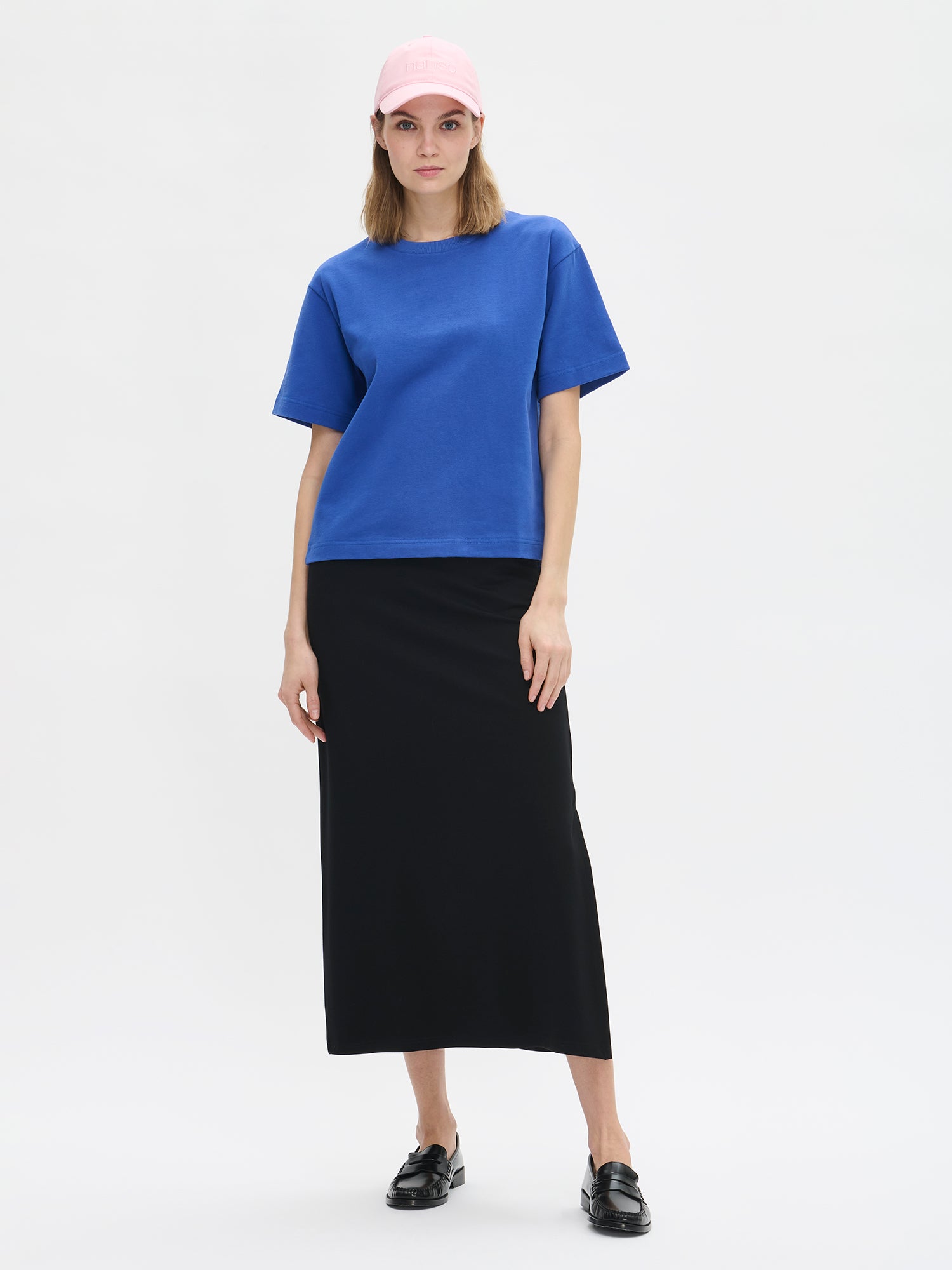 Nanso women's solid blue Forma T-shirt. This boxy, loose-fitting T-shirt features a round ribbed neckline and loose 2/4-length sleeves. On a model with a midi skirt and cap.