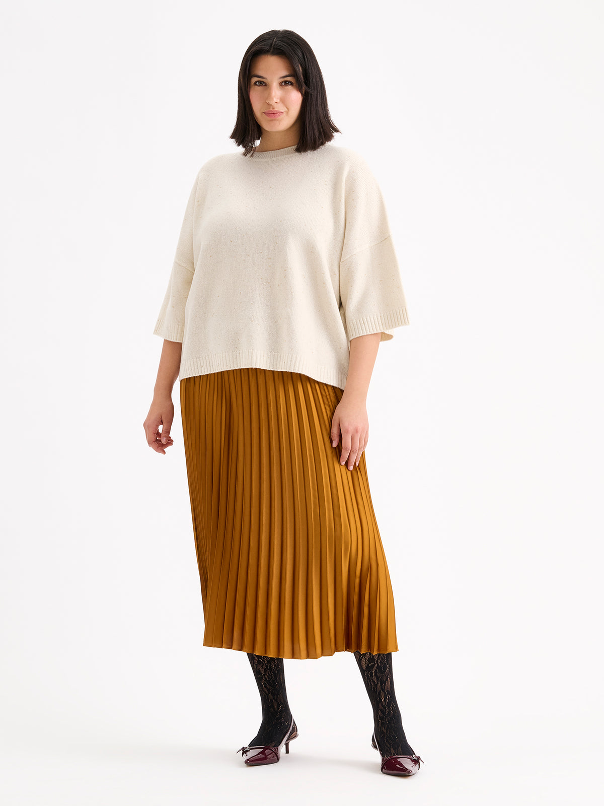 Nanso's elegant Taite skirt for women features a graceful drape in a rich brown shade, pictured on a model with a white half-sleeved sweater.