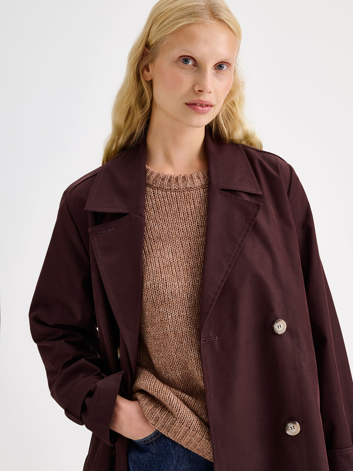 A timeless Brown trench coat on a blonde model, close up.