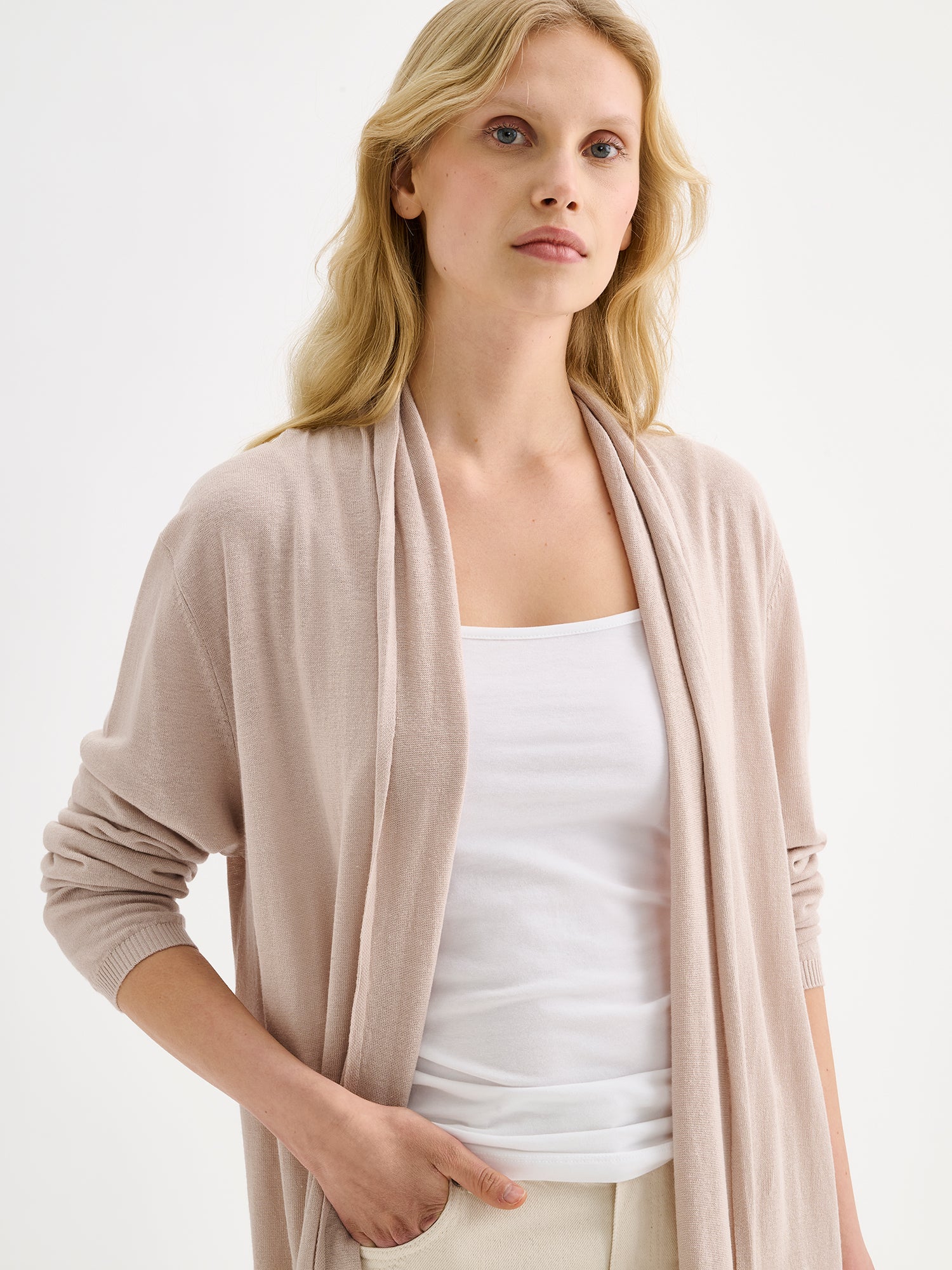 Nanso women's elegant long Karina cardigan in soft and neutral light beige on a model with natural white jeans and a white top, close-up.