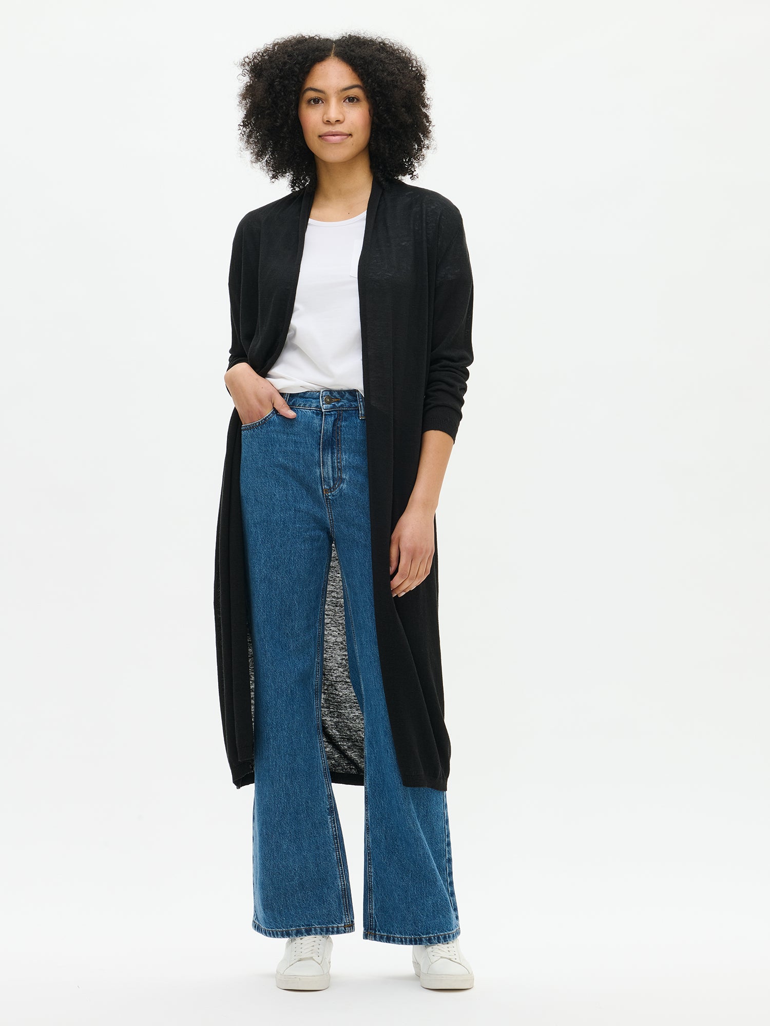 Nanso women's elegant long Karina cardigan in black. Stylish and comfortable cardigan with a shaped knit, classic shawl collar, and full-length sleeves. Pictured on a model with jeans.
