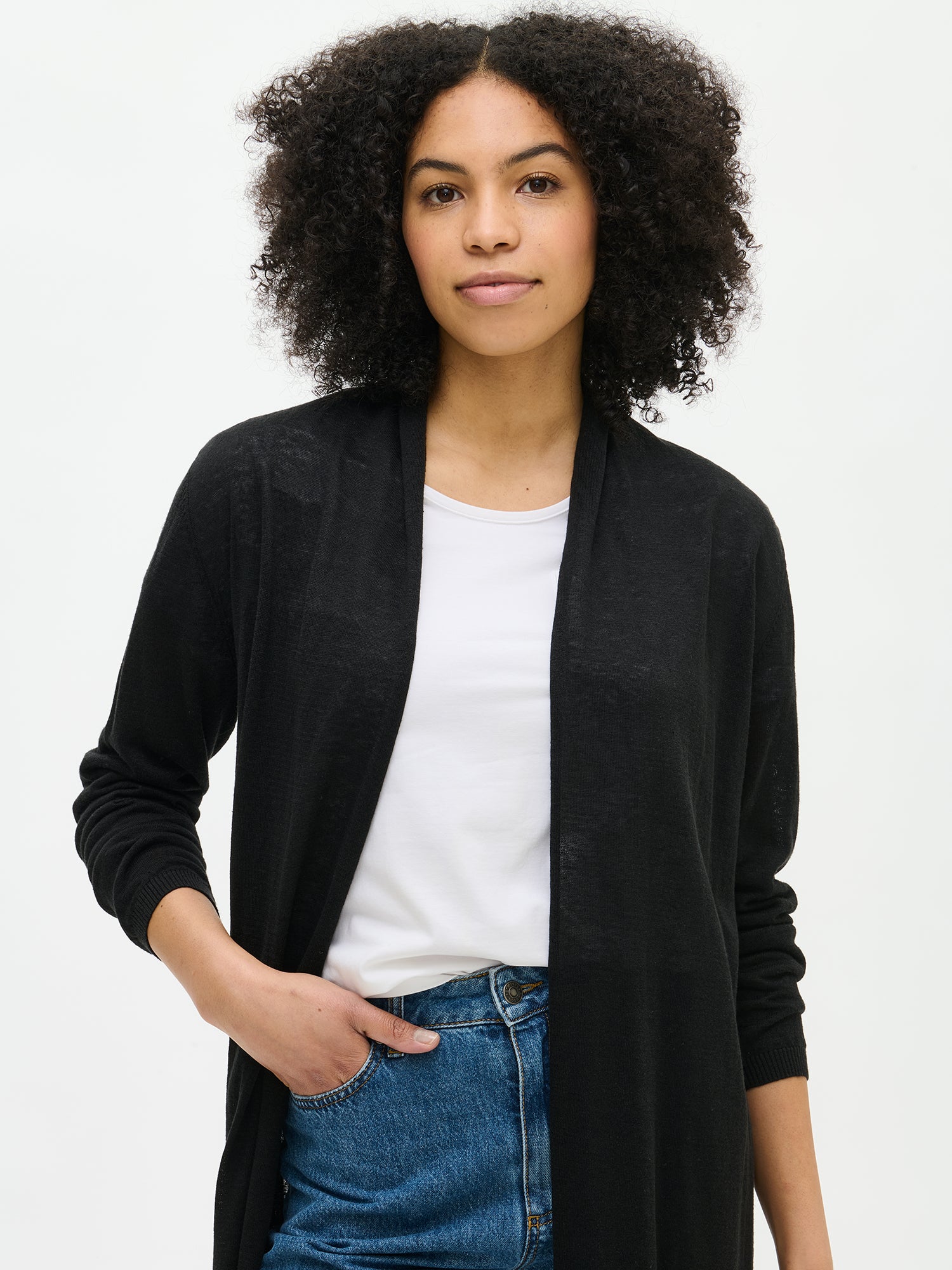 Nanso women's elegant long Karina cardigan in black. Stylish and comfortable cardigan with a shaped knit, classic shawl collar, and full-length sleeves. Pictured on a model with jeans, close-up.