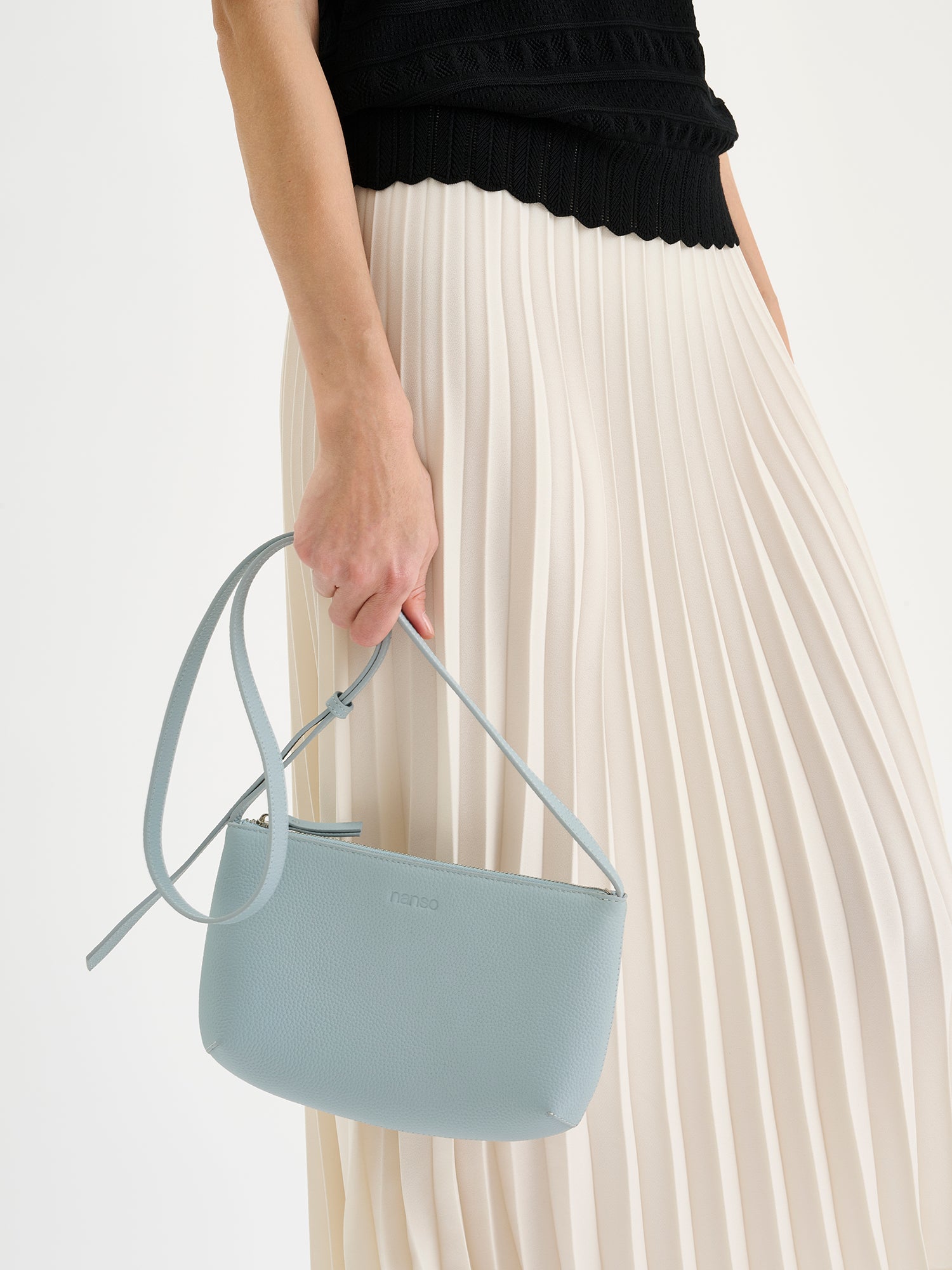 Nanso sleek light blue Naru leather bag comes with a long, adjustable shoulder strap and a secure zip closure. Made from certified leather. Pictured on a model with a pleated skirt