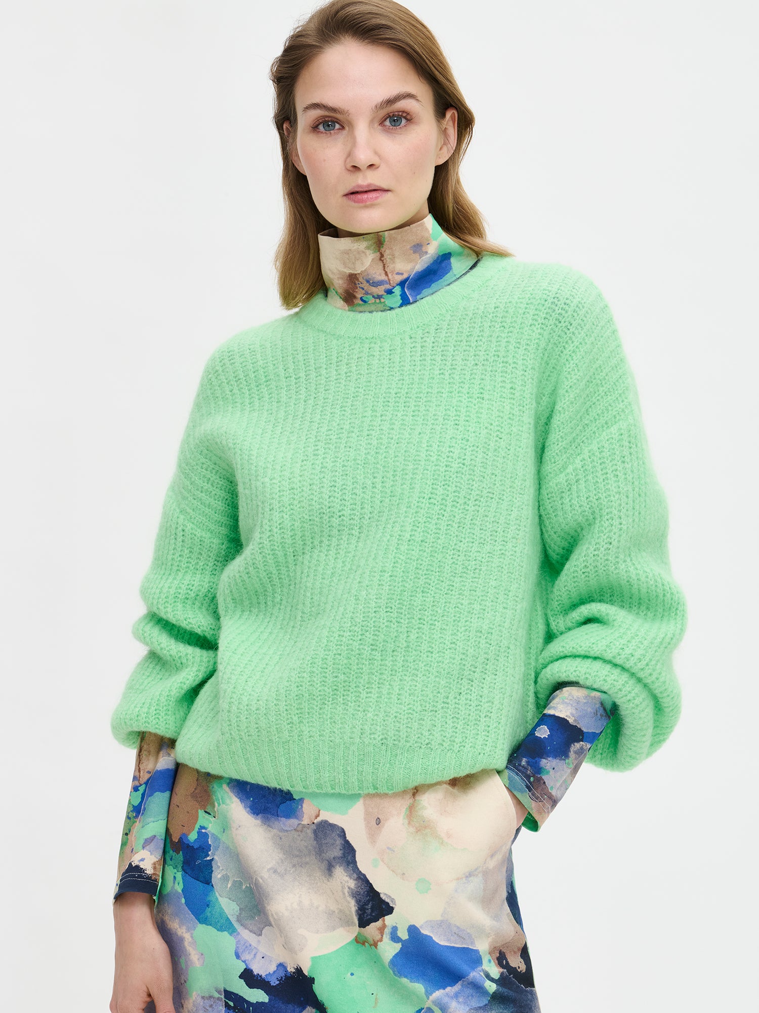 KARAMELLI women's luxurious mohair blend Knit Sweater in light green shade features a round neckline and full-length sleeves. Pictured on a model with a patterned dress, close-up.