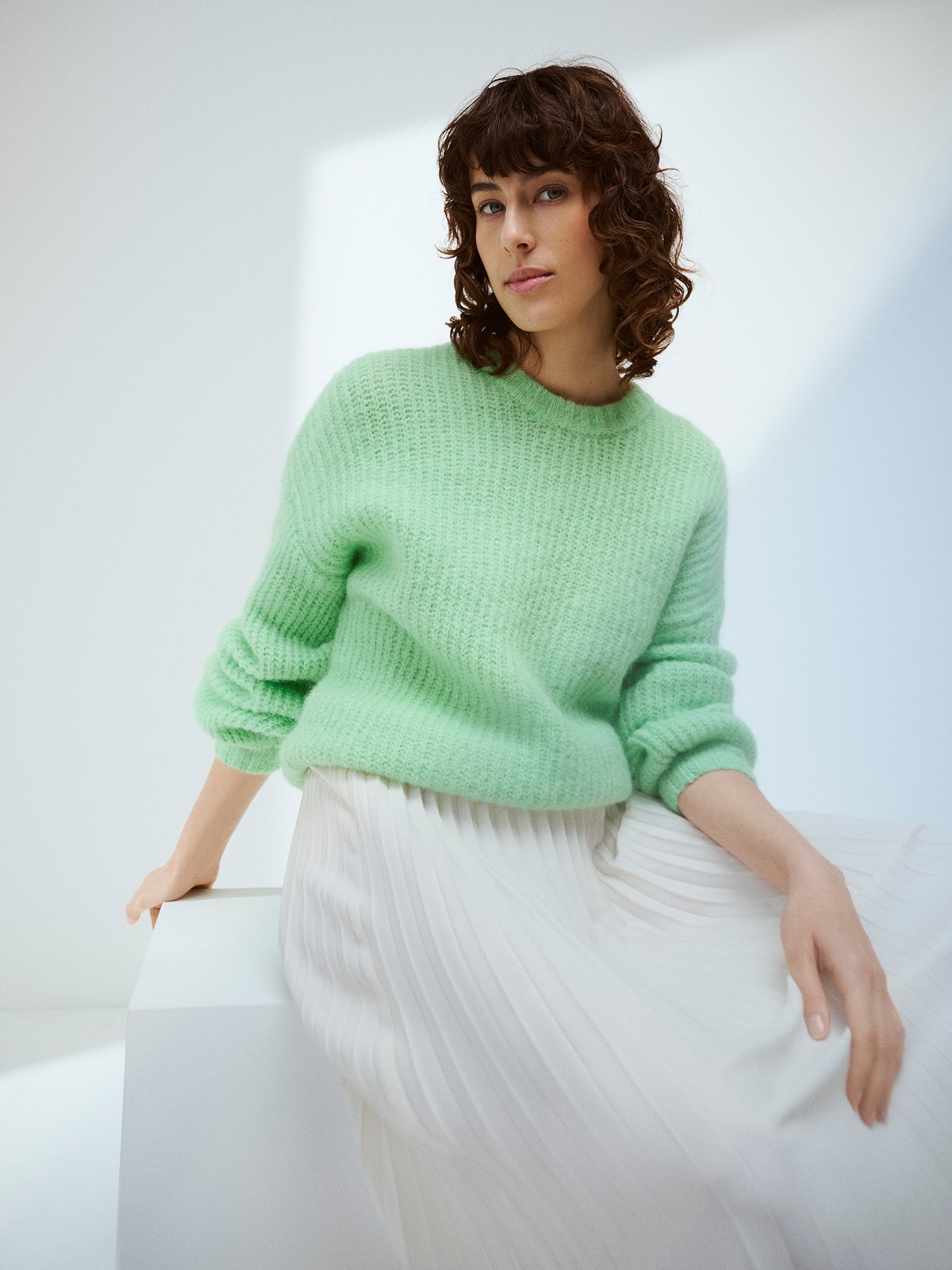 KARAMELLI women's luxurious mohair blend Knit Sweater in light green shade features a round neckline and full-length sleeves. Pictured on a model with a white skirt.