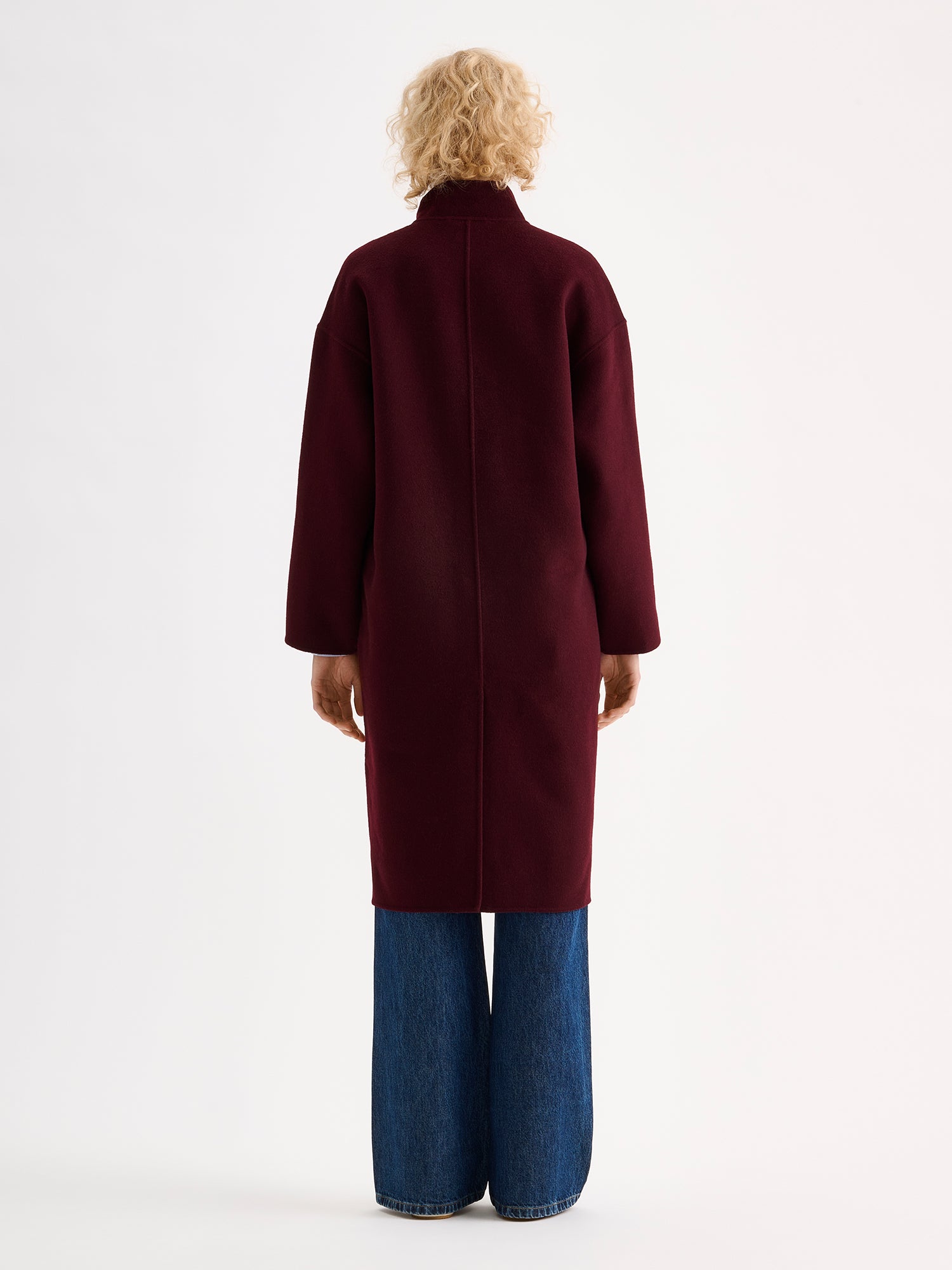 Nanso women's long burgundy Elle wool coat on a blonde model with blue jeans, from the backside