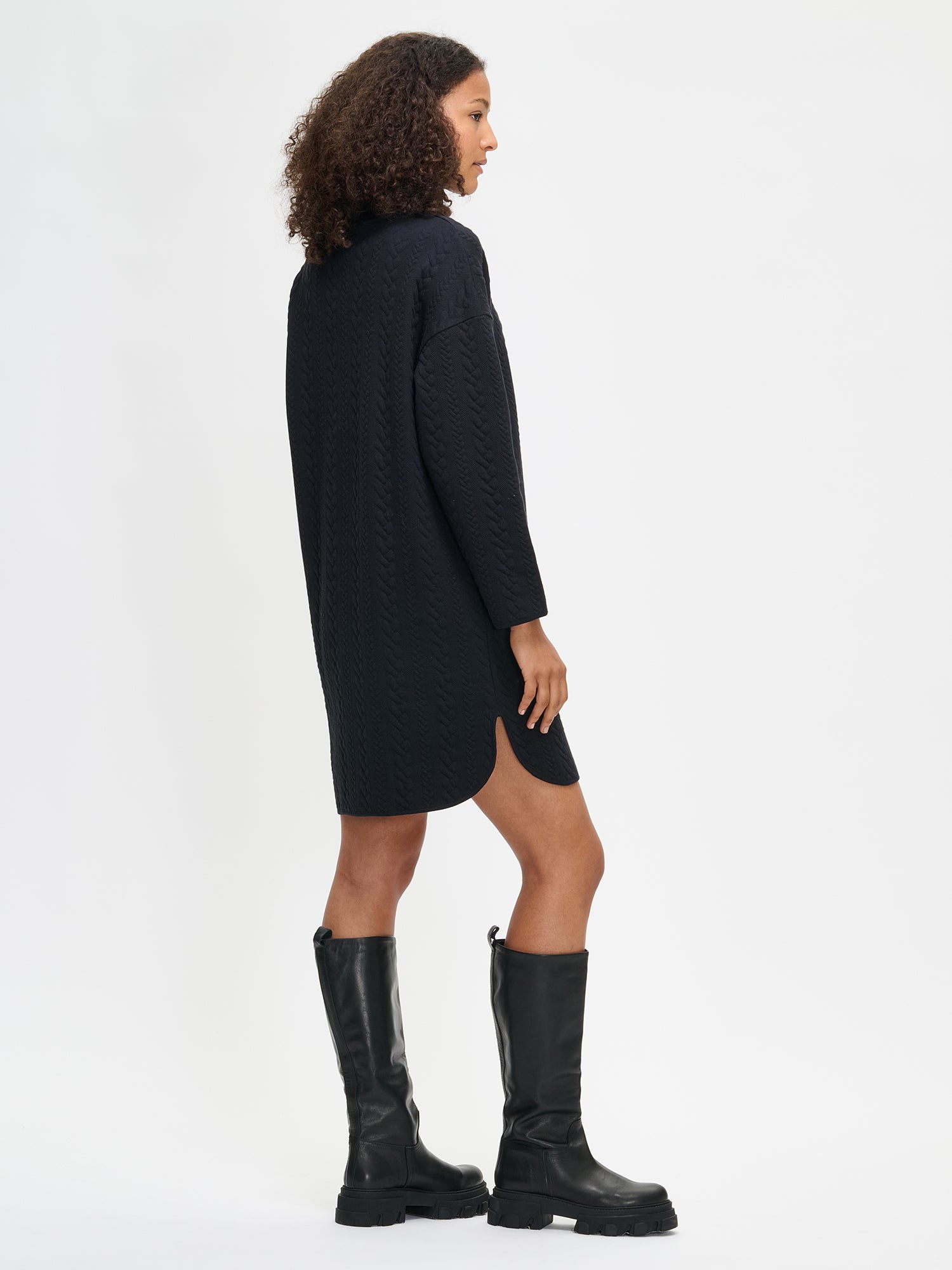 Woman wearing a black dress and black boots on a white background