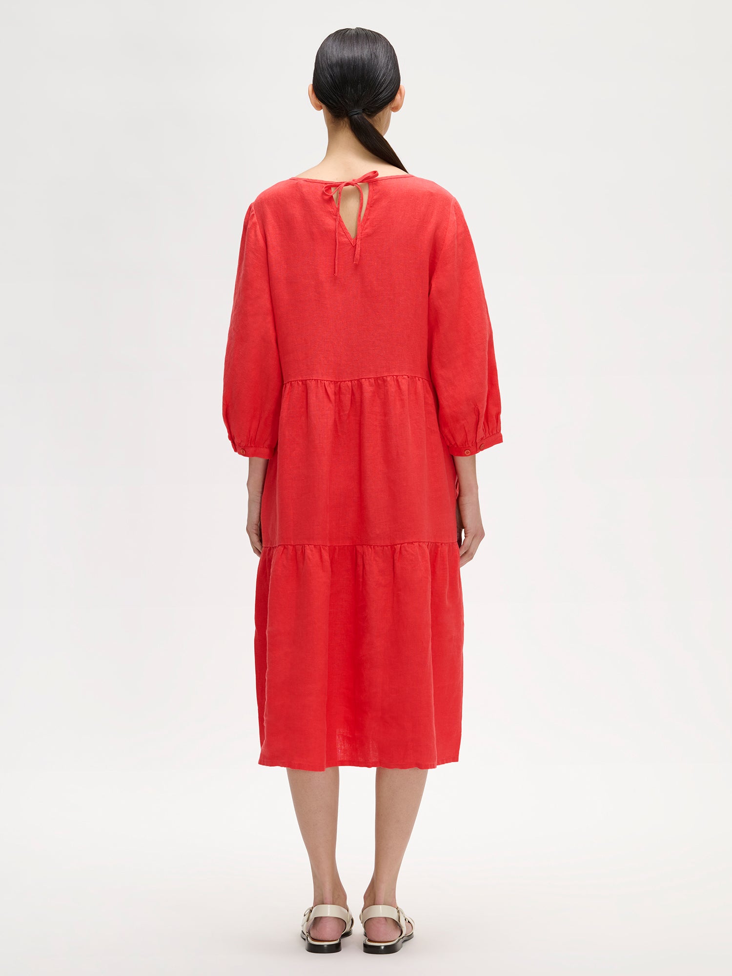 Women's Saralia Linen Dress in red with voluminous frill layers on a model with sandals, photographed from the backside.