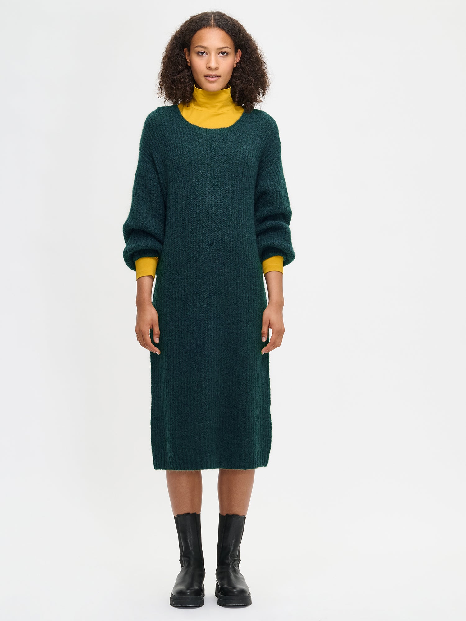 Woman wearing a green Karamelli sweater dress with a yellow turtleneck underneath