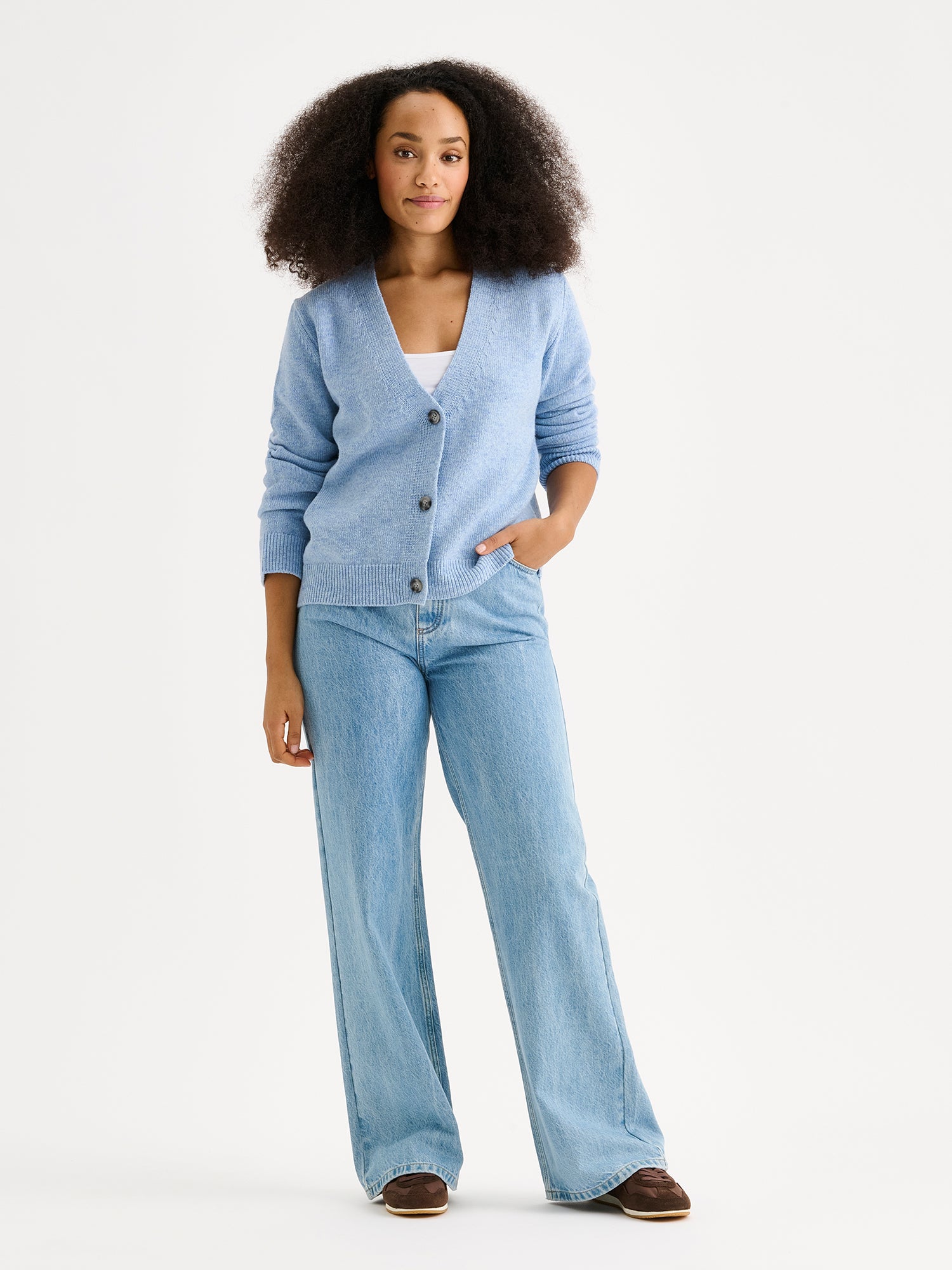 The LANA long-sleeved Knit Cardigan in blue with a flattering V-neckline and button closure down the front. On a model with jeans and sneakers.