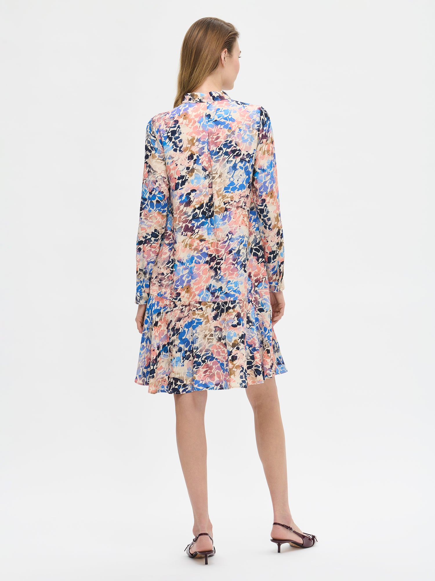 Women's SAGITTA Dress with vibrant pattern and flared hem. The dress features a front button closure and timeless collar design, paired with full-length sleeves. Pictured from the backside on a model with high heels.