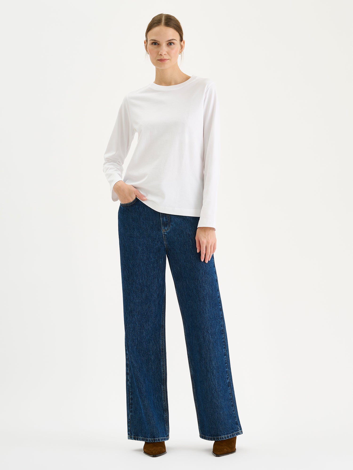 Nanso womens white NORMI Long-Sleeved T-Shirt is a versatile piece that features a classic crew neckline and full-length sleeves for everyday versatility. Pictured on a model with blue jeans.