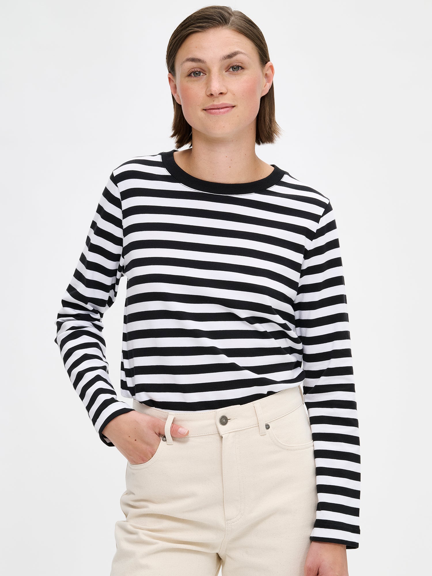 The RAITA NORMI Long-Sleeved Shirt in black and white featuring striped pattern. The straight-cut shirt features a round neckline and full-length sleeves. 100% organic cotton. Pictured on a model with jeans, close-up.