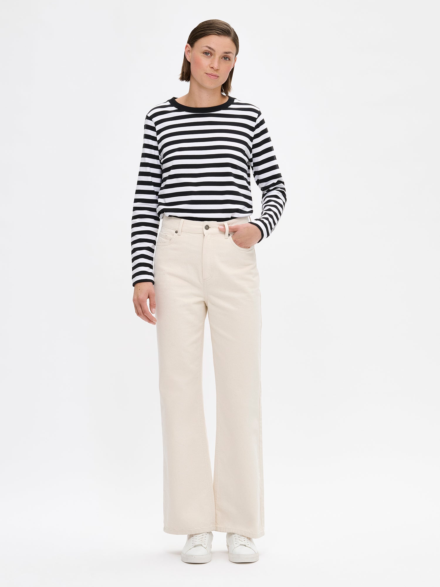 The RAITA NORMI Long-Sleeved Shirt in black and white featuring striped pattern. The straight-cut shirt features a round neckline and full-length sleeves. 100% organic cotton. Pictured on a model with jeans.