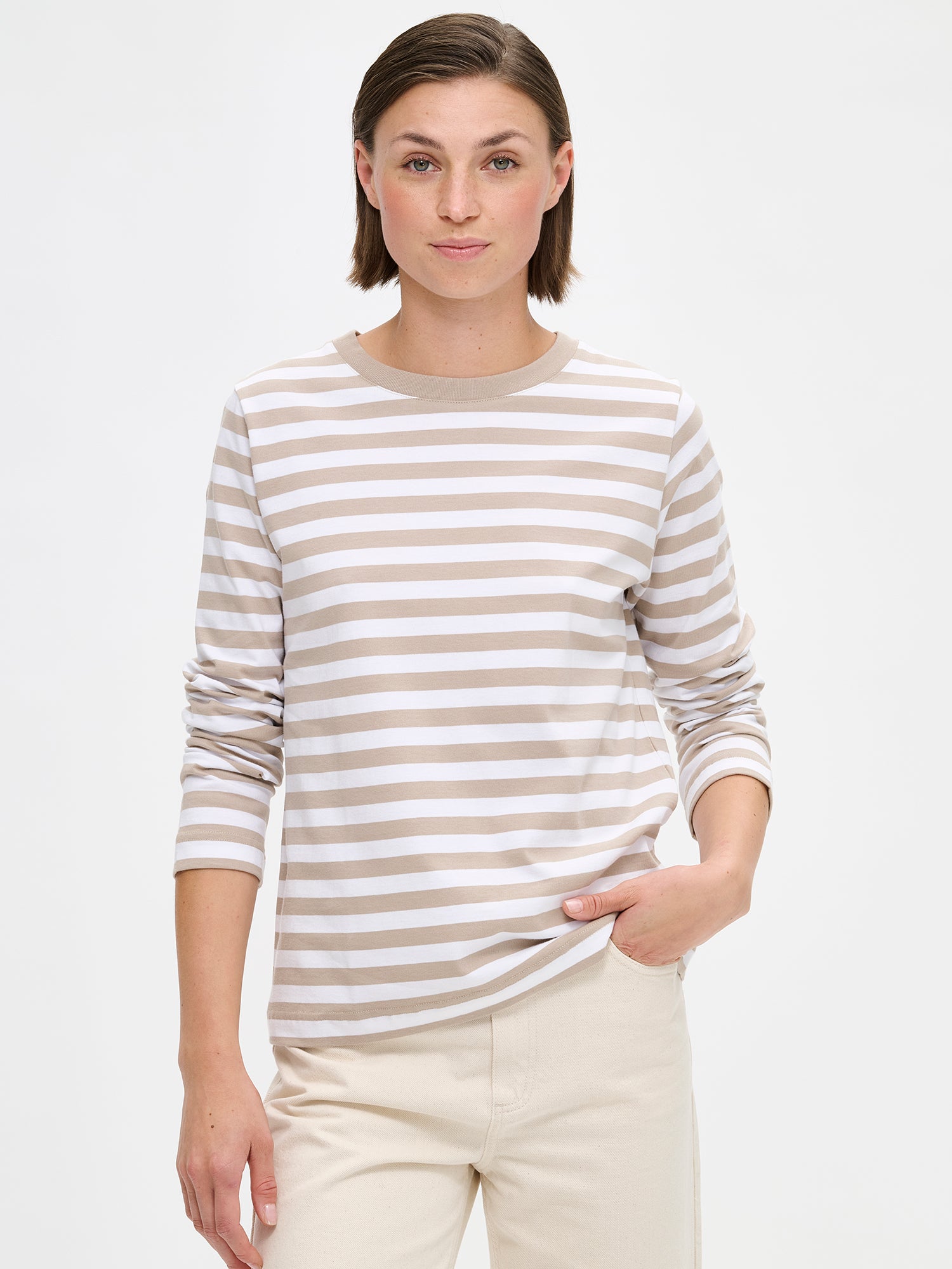 The RAITA NORMI Long-Sleeved Shirt in beige featuring striped pattern. The straight-cut shirt features a round neckline and full-length sleeves. 100% organic cotton. Pictured on a model with jeans, close-up.