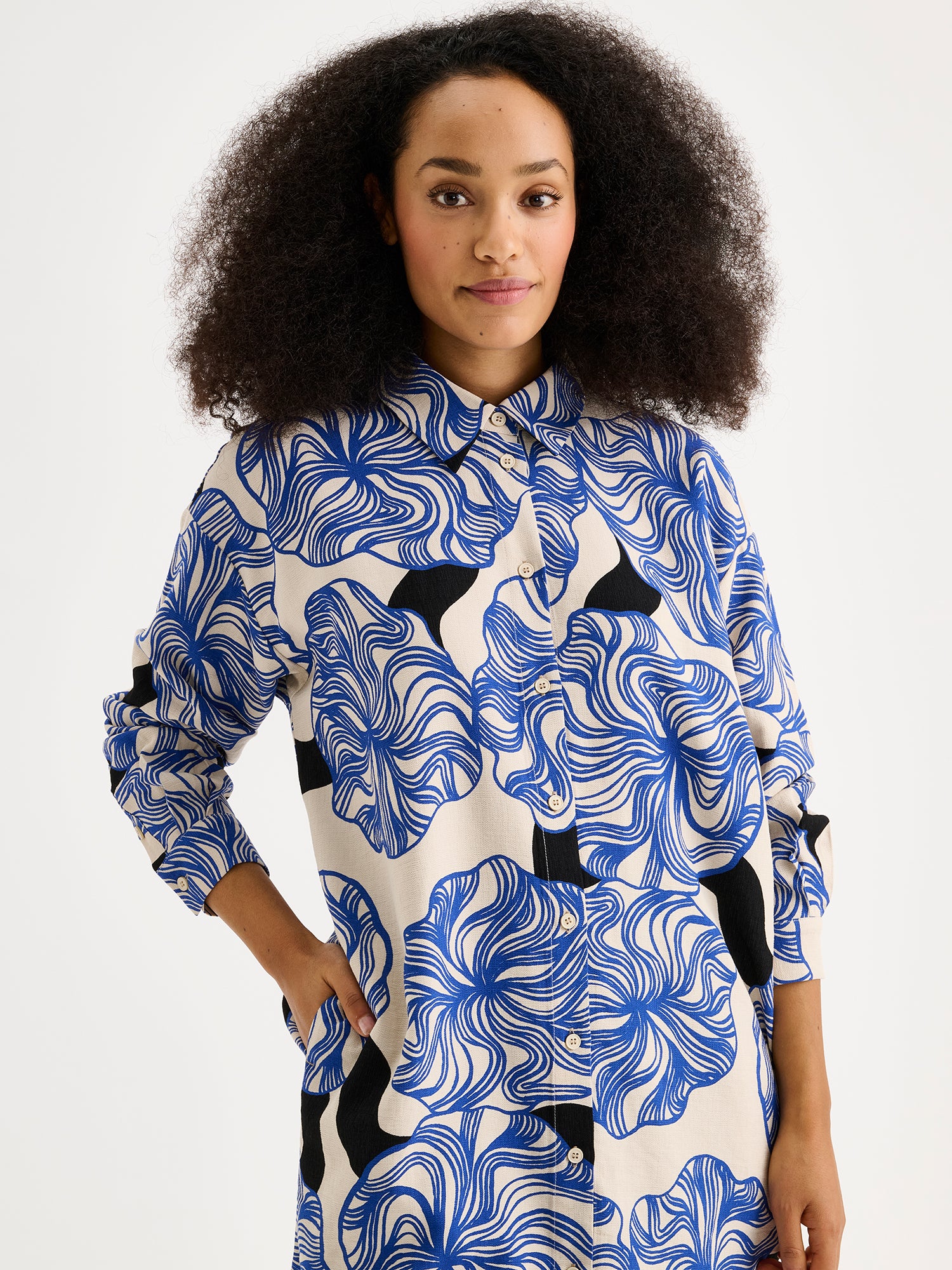 Women's KOSMO shirt features a striking blue patterned design paired with a timeless collar style, full-length sleeves, a practical front button closure and side pockets. On a model, close-up.