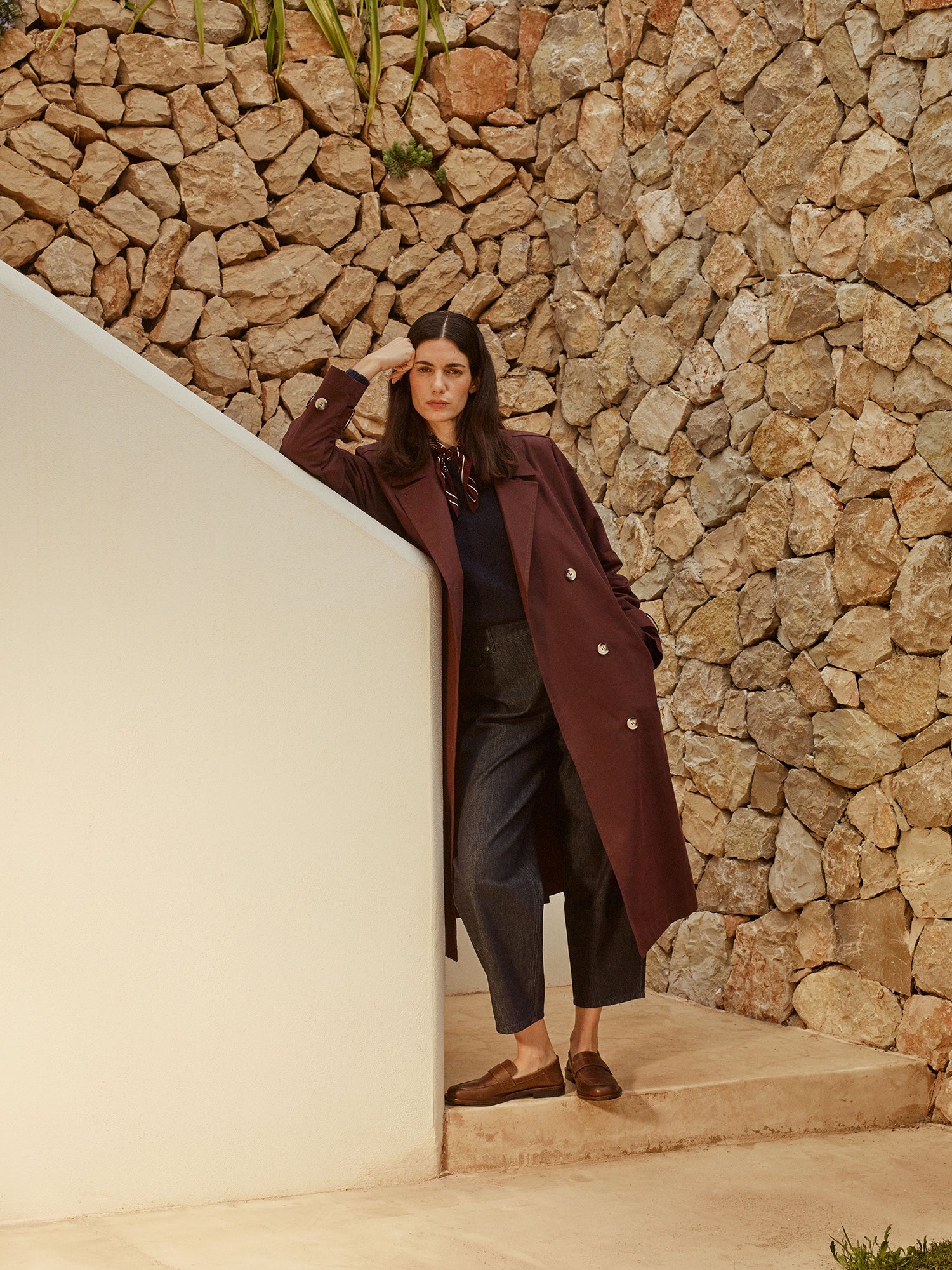 Nanso women's relaxed barrel leg Rento jeans in dark blue with an effortlessly comfortable fit, on a model with a dark brown trench coat, brown silk scarf and loafers
