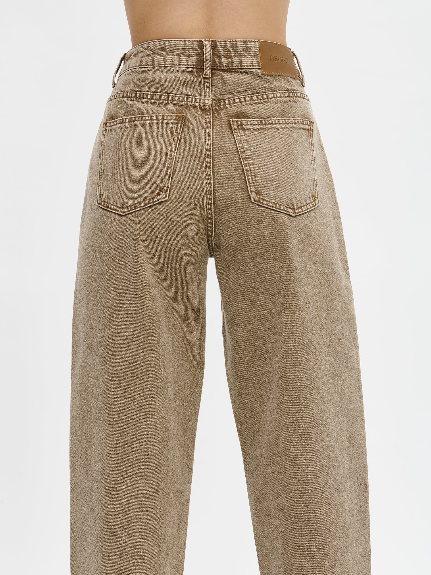 Nanso women's relaxed barrel leg Rento jeans in brown with an effortlessly comfortable fit.
Classic five-pocket design with a mid-rise waistband, front zip and button closure. On a model from the back, close-up.