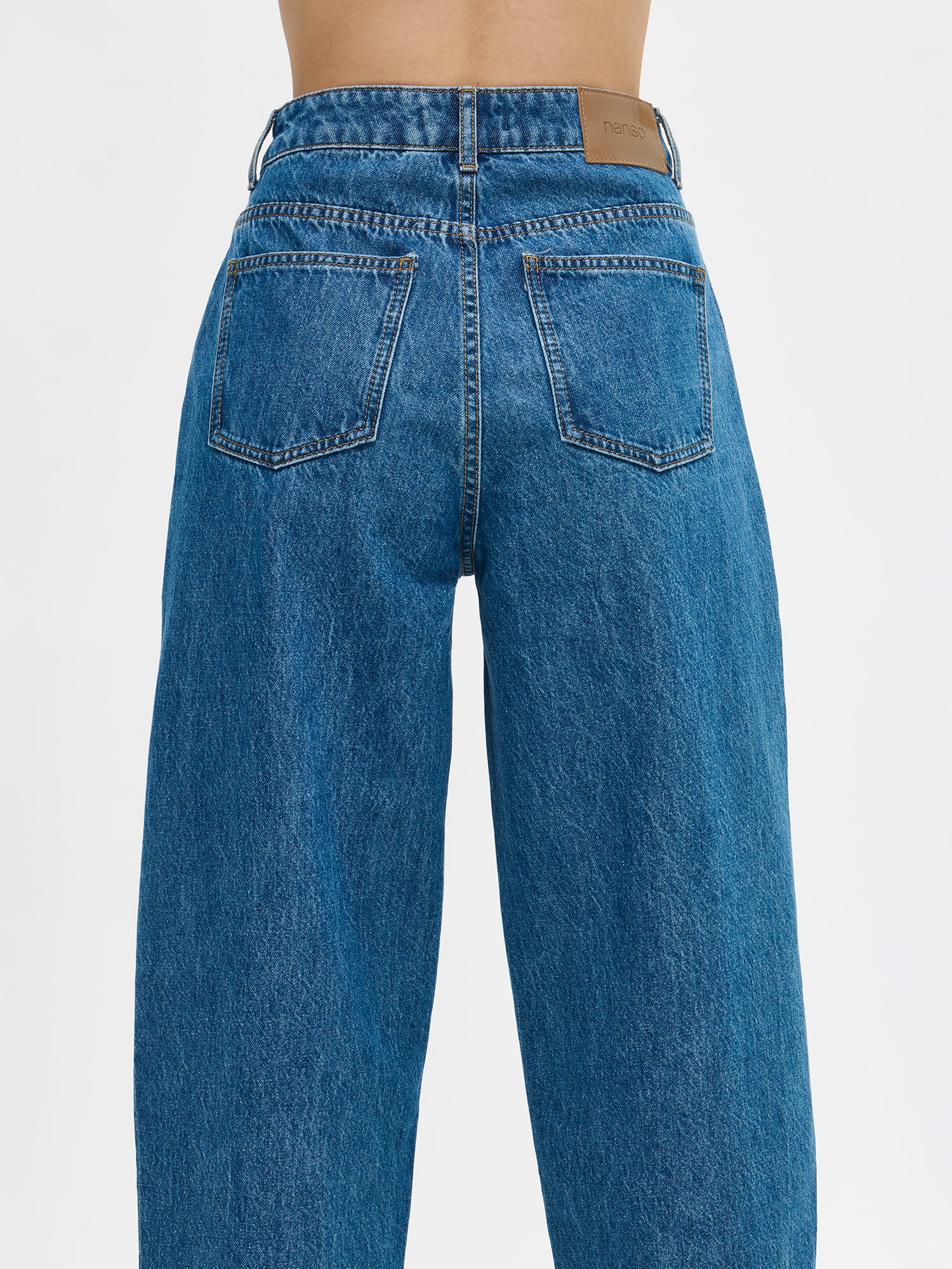 Nanso women's relaxed barrel leg Rento jeans in blue with an effortlessly comfortable fit.
Classic five-pocket design with a mid-rise waistband, front zip and button closure. On a model from the back, close-up.
